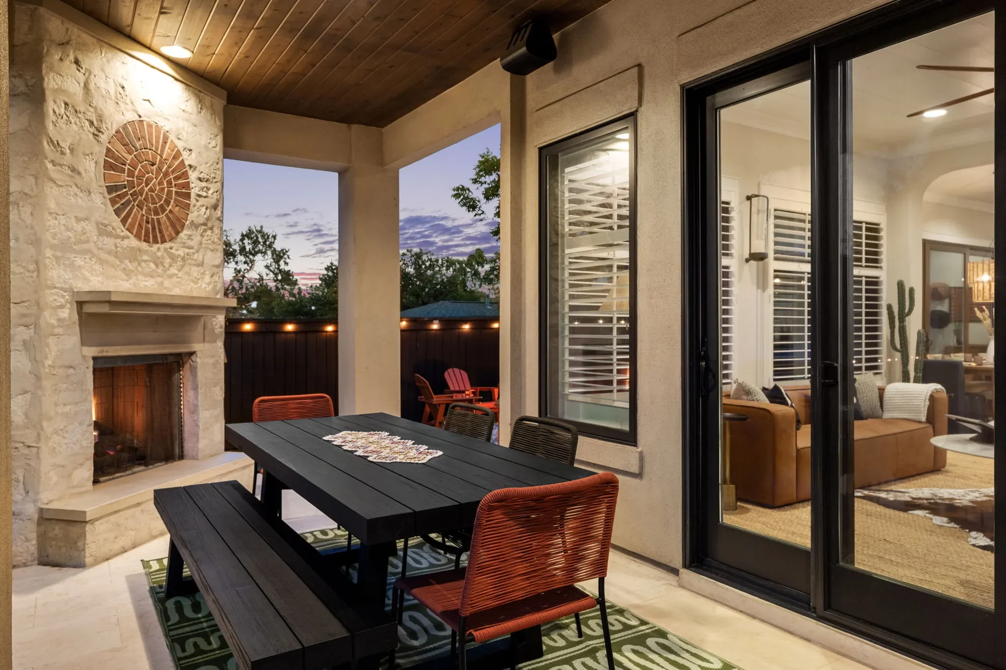 Patio with a black outdoor dining table, bench and chairs, and a fireplace next to a patio door that opens into the interior.
