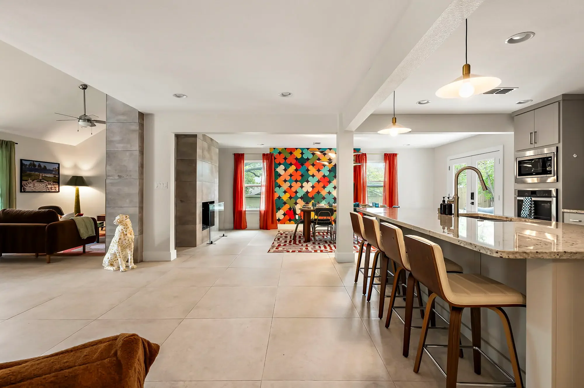 Short-term rental open plan kitchen and dining design with gray island, bold floral mural wall, red curtains, and dalmatian statue — Austin TX.