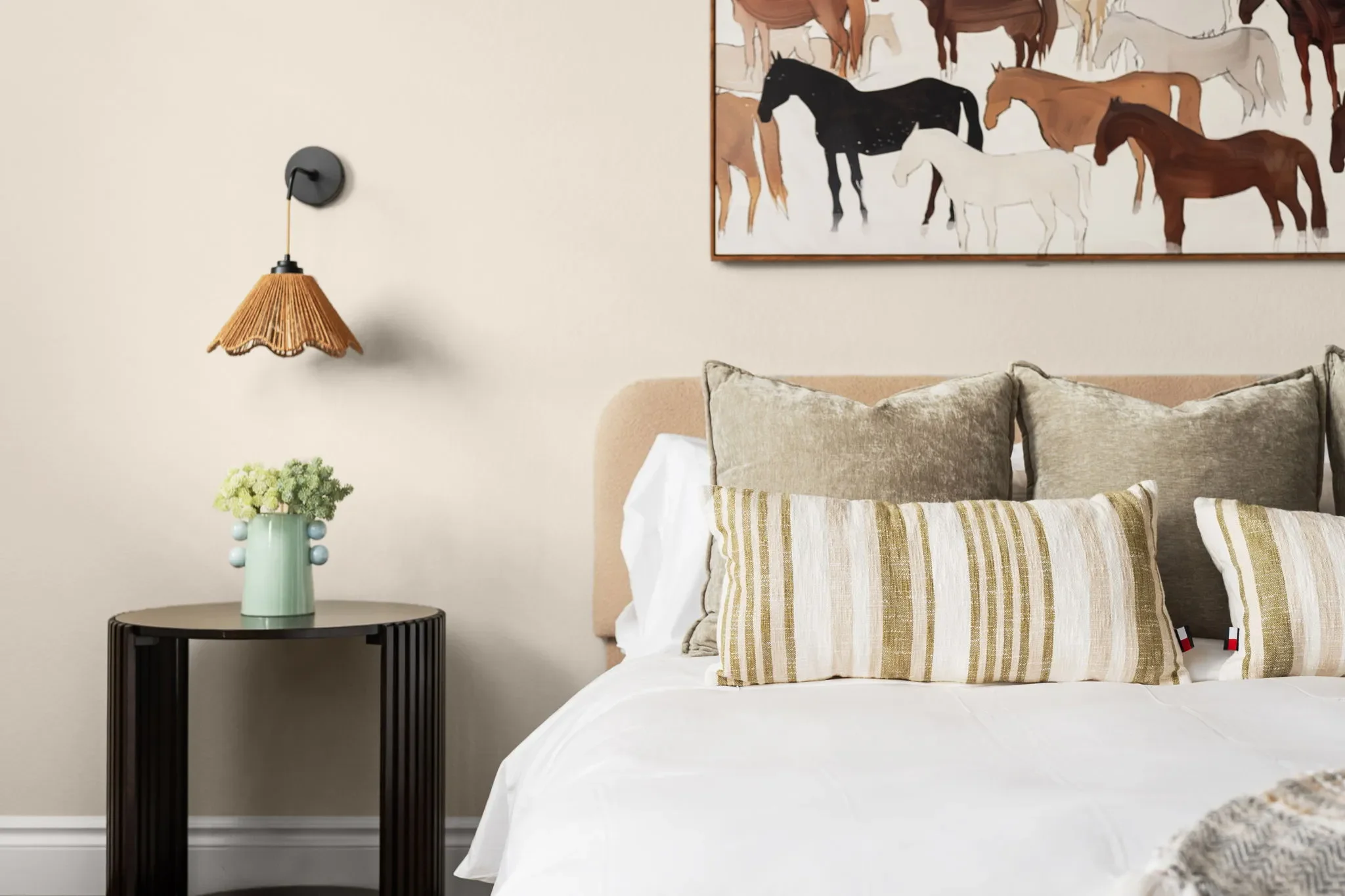 Bed featuring horse wall art, boho rattan wall sconces, a large wooden nightstand, and layered decorative pillows.