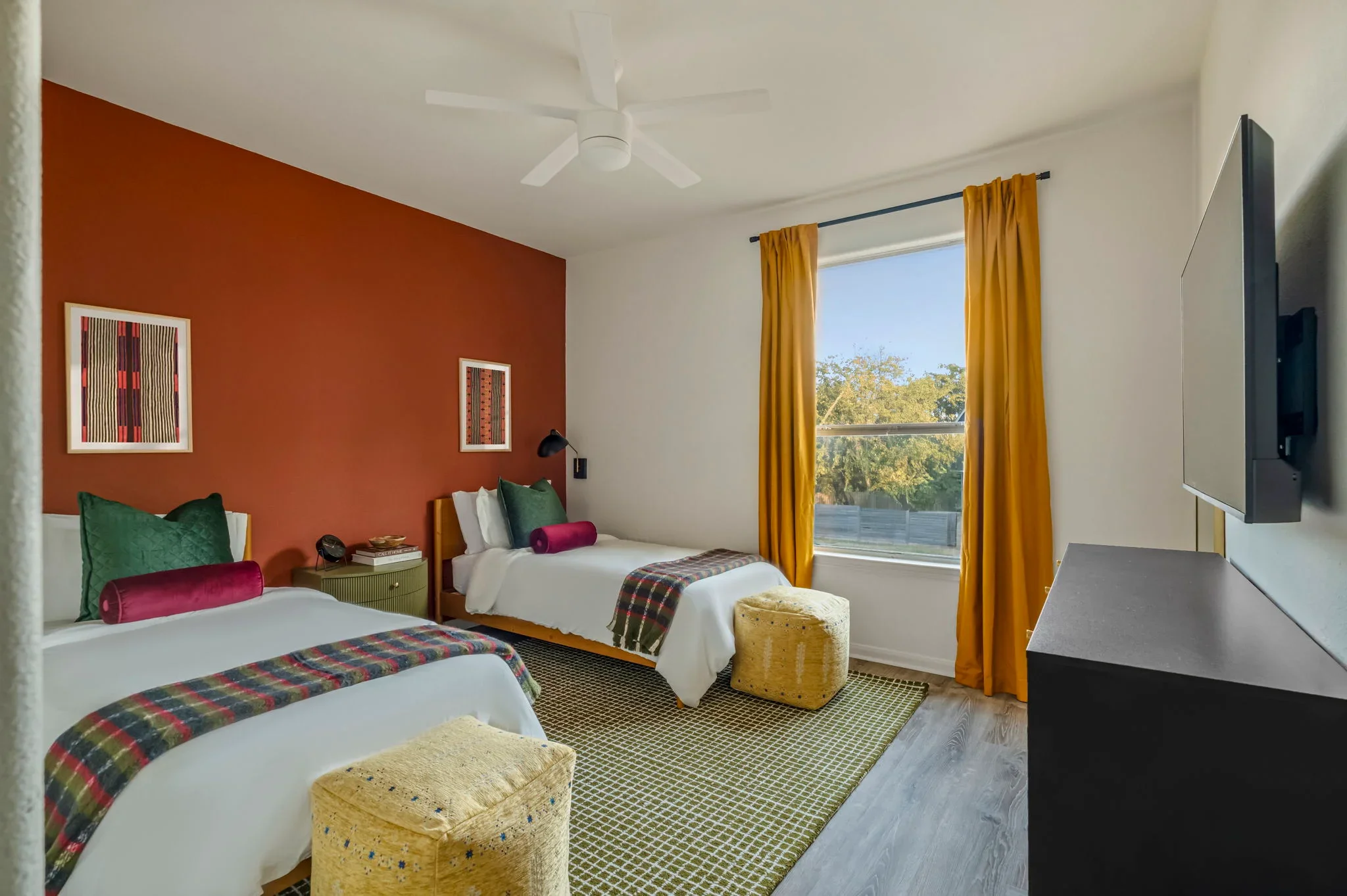 Short-term rental double bedroom design with terracotta accent wall, two beds, green velvet pillows, and mustard curtains — Austin TX.