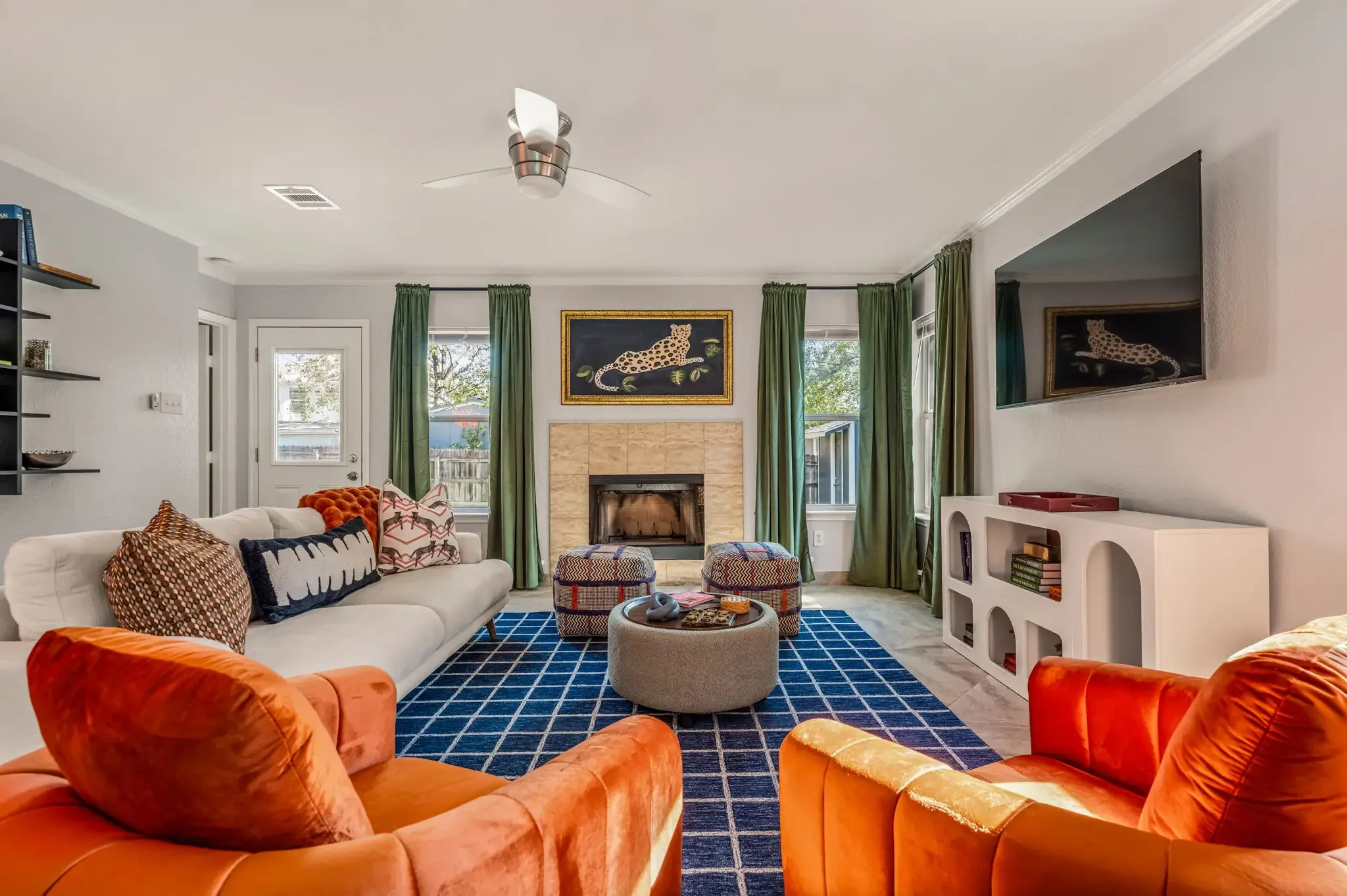 Airbnb living room design with orange sofas, blue grid rug, fireplace, and built-in shelving — Austin TX.