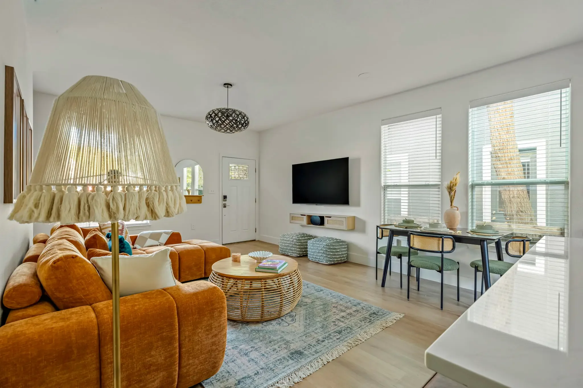 Airbnb living room design with rust velvet sectional, fringe floor lamp, rattan coffee table, and view to dining area — Austin TX.
