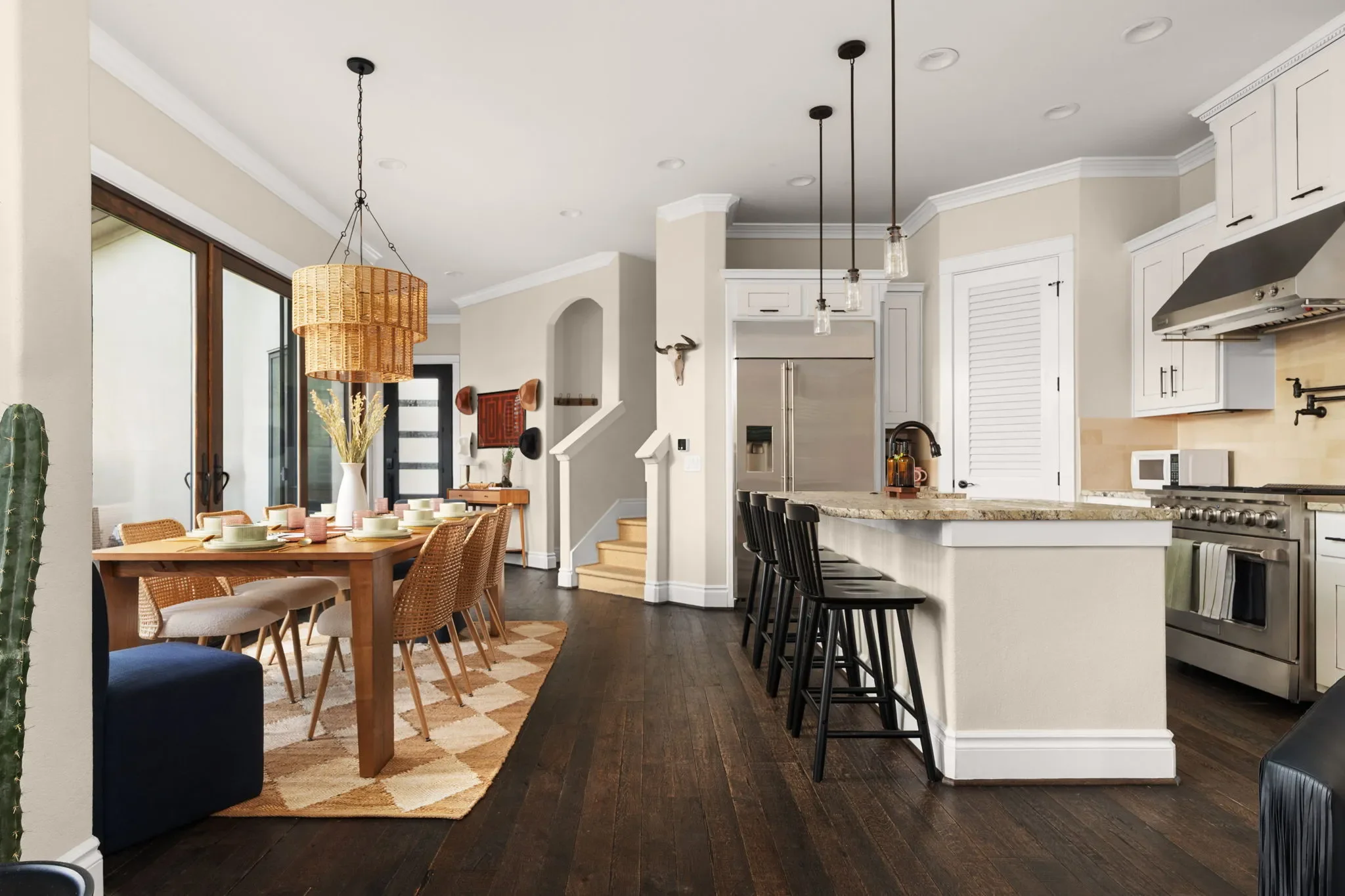 Dining room with a rattan pendant light, large wooden dining table, cowboy hat feature wall, and a kitchen island with black wooden barstools.