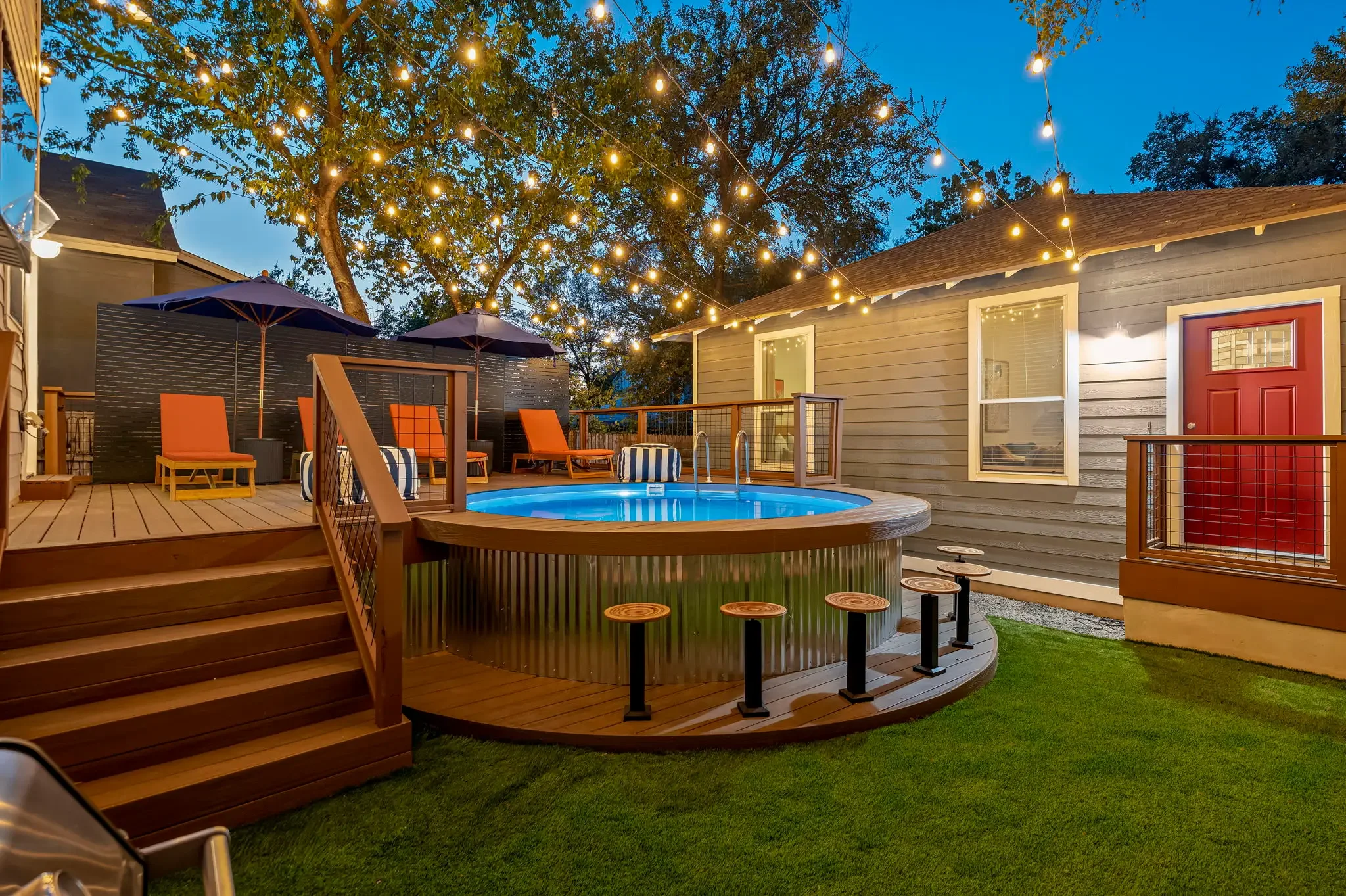 Short-term rental backyard design with round above-ground pool, swim-up bar stools, string lights, and orange lounge chairs at dusk — Austin TX.