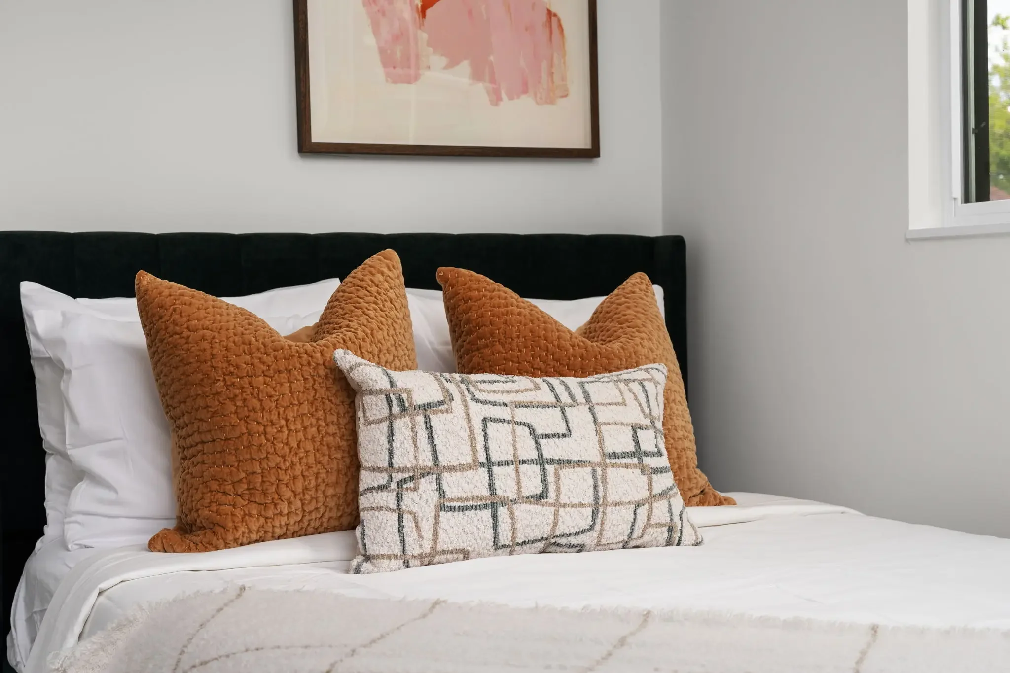 Short-term rental bedroom design detail with black velvet tufted headboard, rust orange pillows, and pink abstract wall art — Austin TX.
