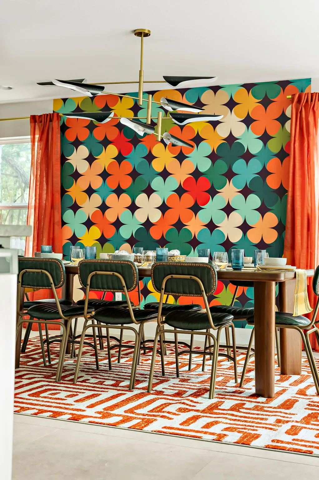 Dining room in a short-term rental with green leather mid-century modern chairs, wooden dining table, red floor-to-ceiling curtains, modern pendant light, and red geometric area rug.