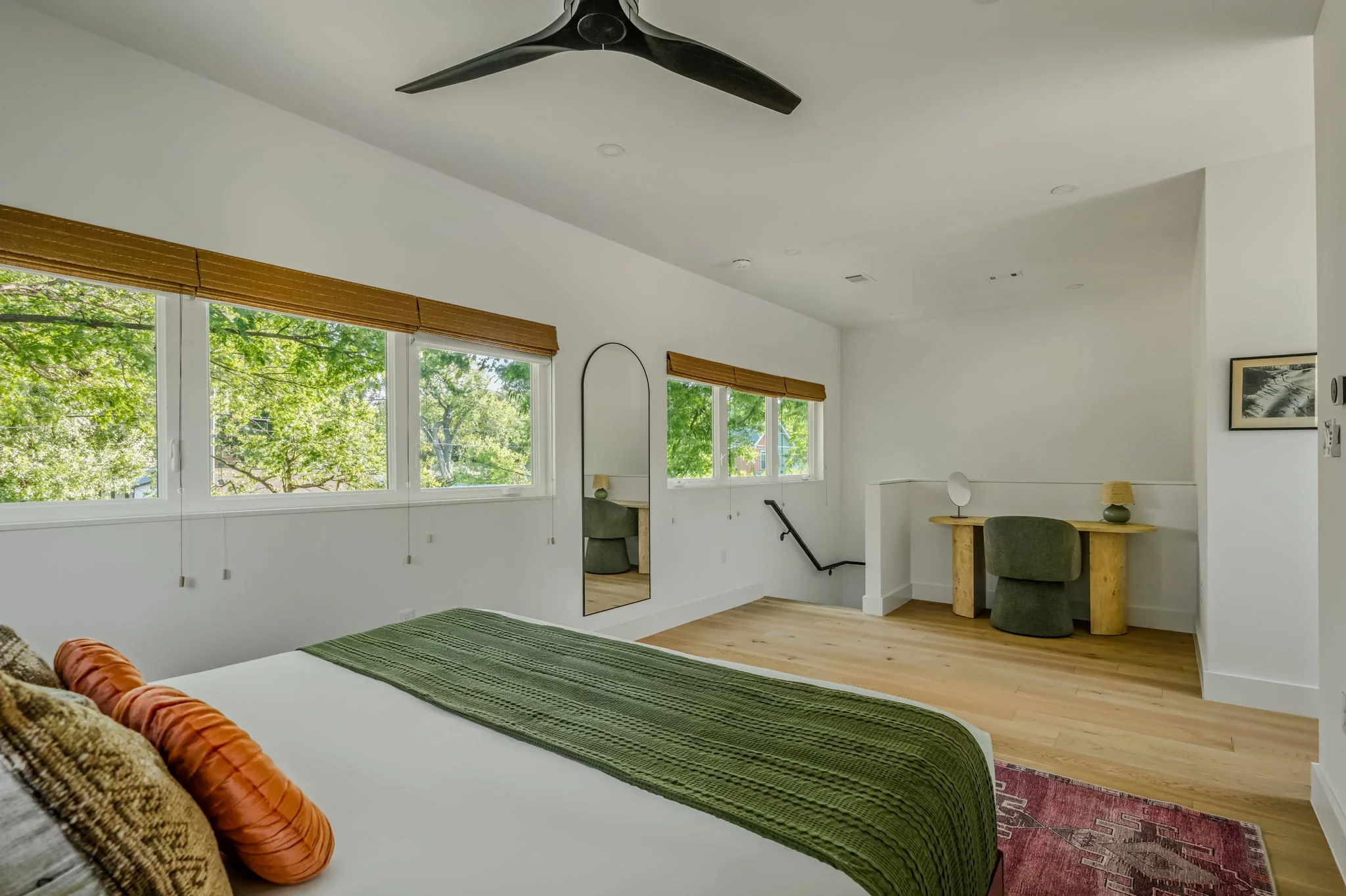 Airbnb primary bedroom design with vaulted ceiling, large windows, green throw, arched mirror, and sitting area with accent chair — Austin TX.