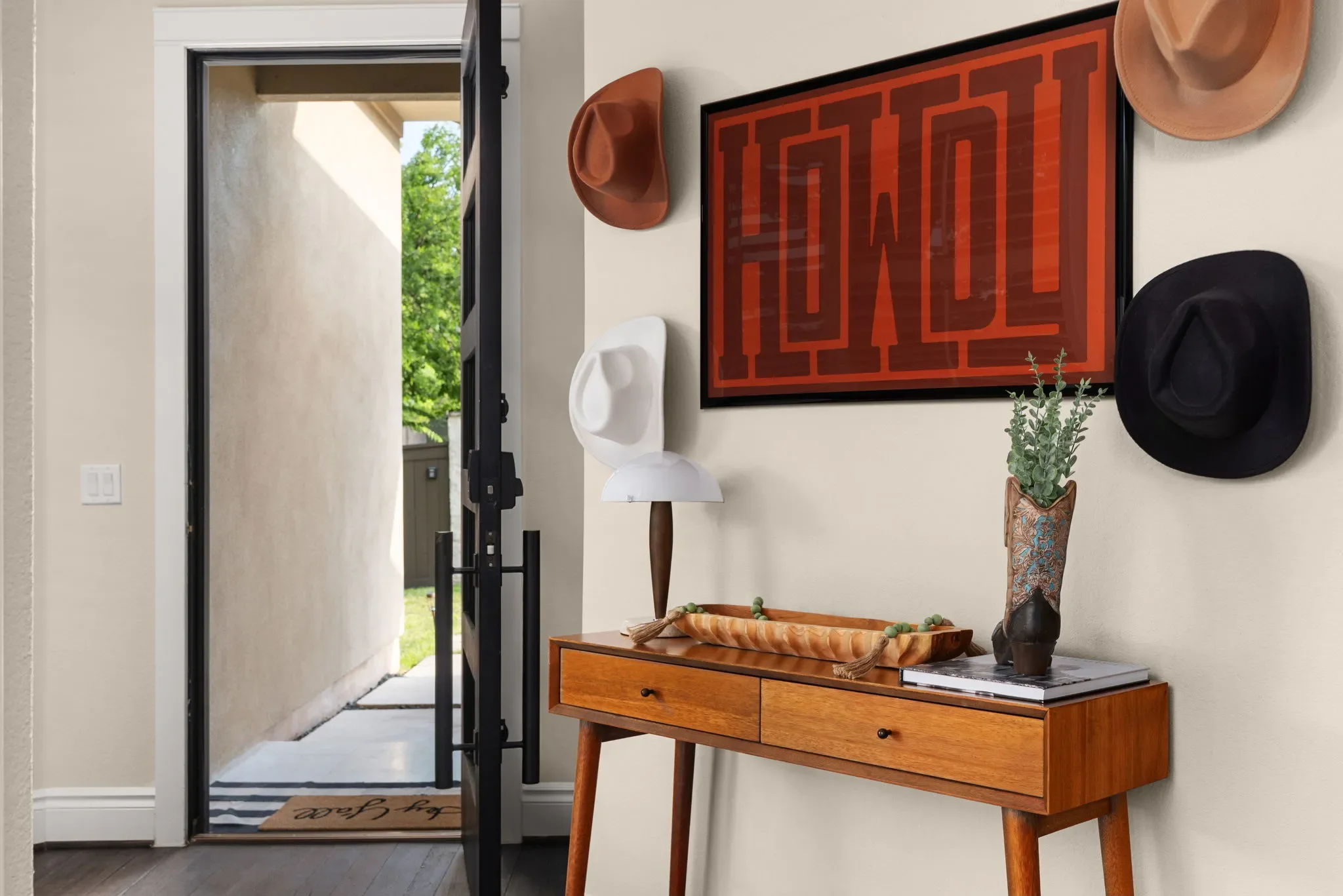 Short-term rental entryway with modern western decor, Howdy wall art, cowboy hats, and console table — Austin TX.