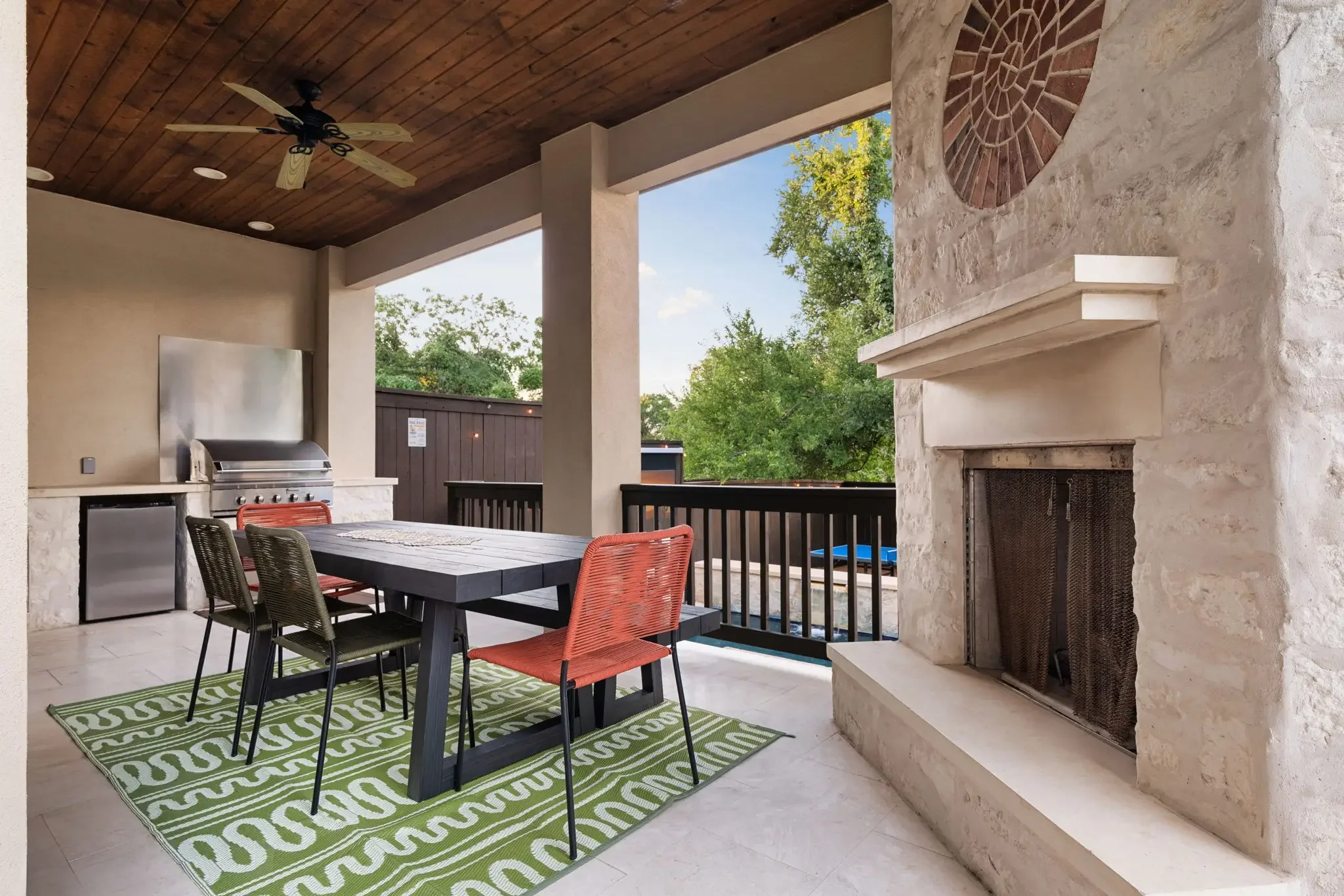 Airbnb outdoor design with covered patio, stone fireplace, outdoor kitchen, black dining table, and red chairs — Austin TX