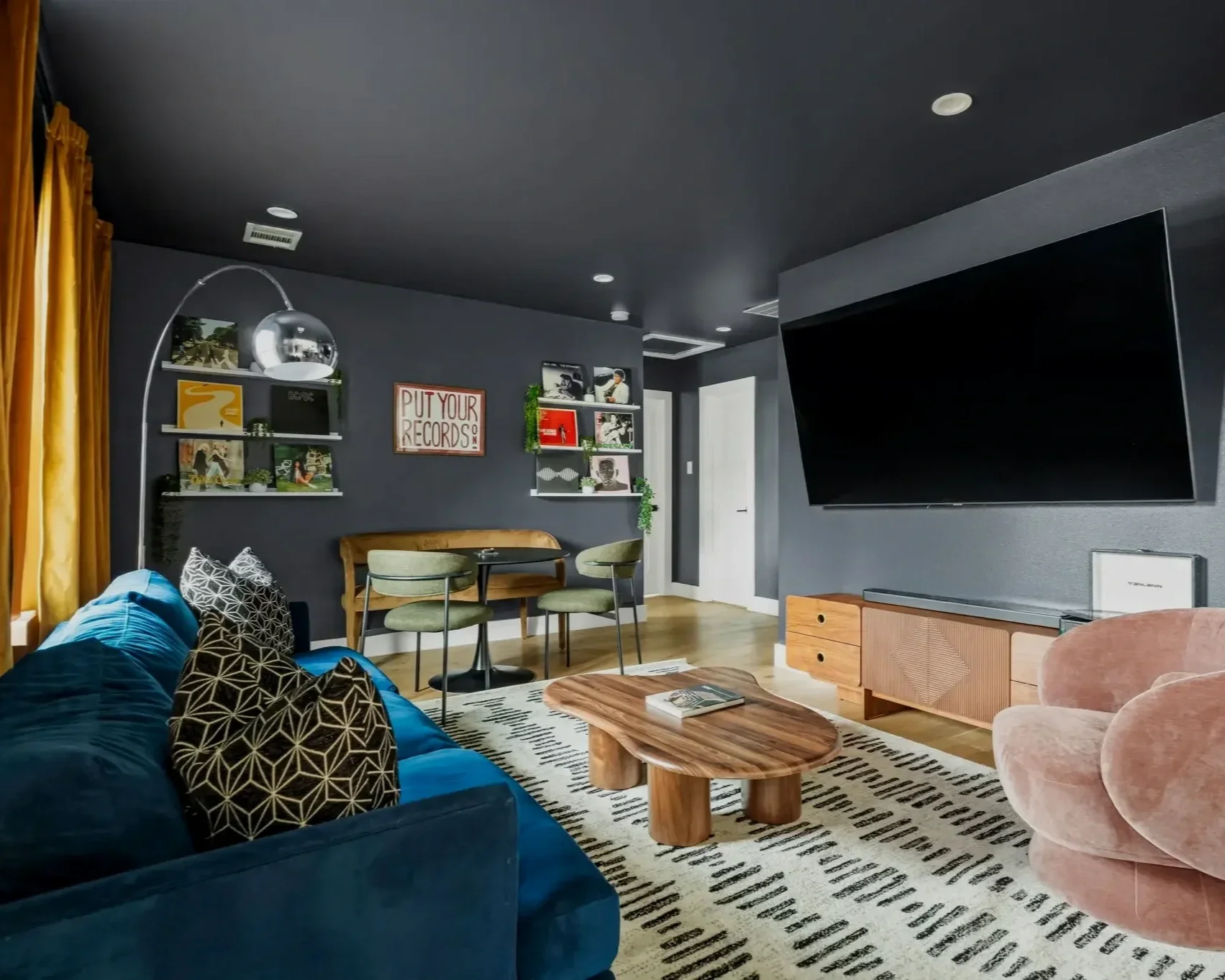 Moody media room with dark walls, blue velvet sofa, custom shelving, statement lighting, and lounge seating inspired by music and art.