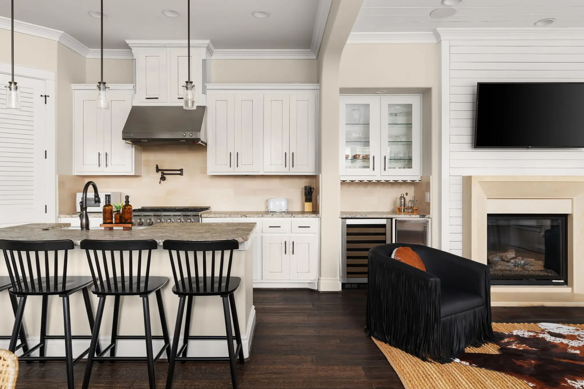 Short-term rental kitchen design with white cabinets, black bar stools, wine fridge, and living room fireplace — Austin TX.