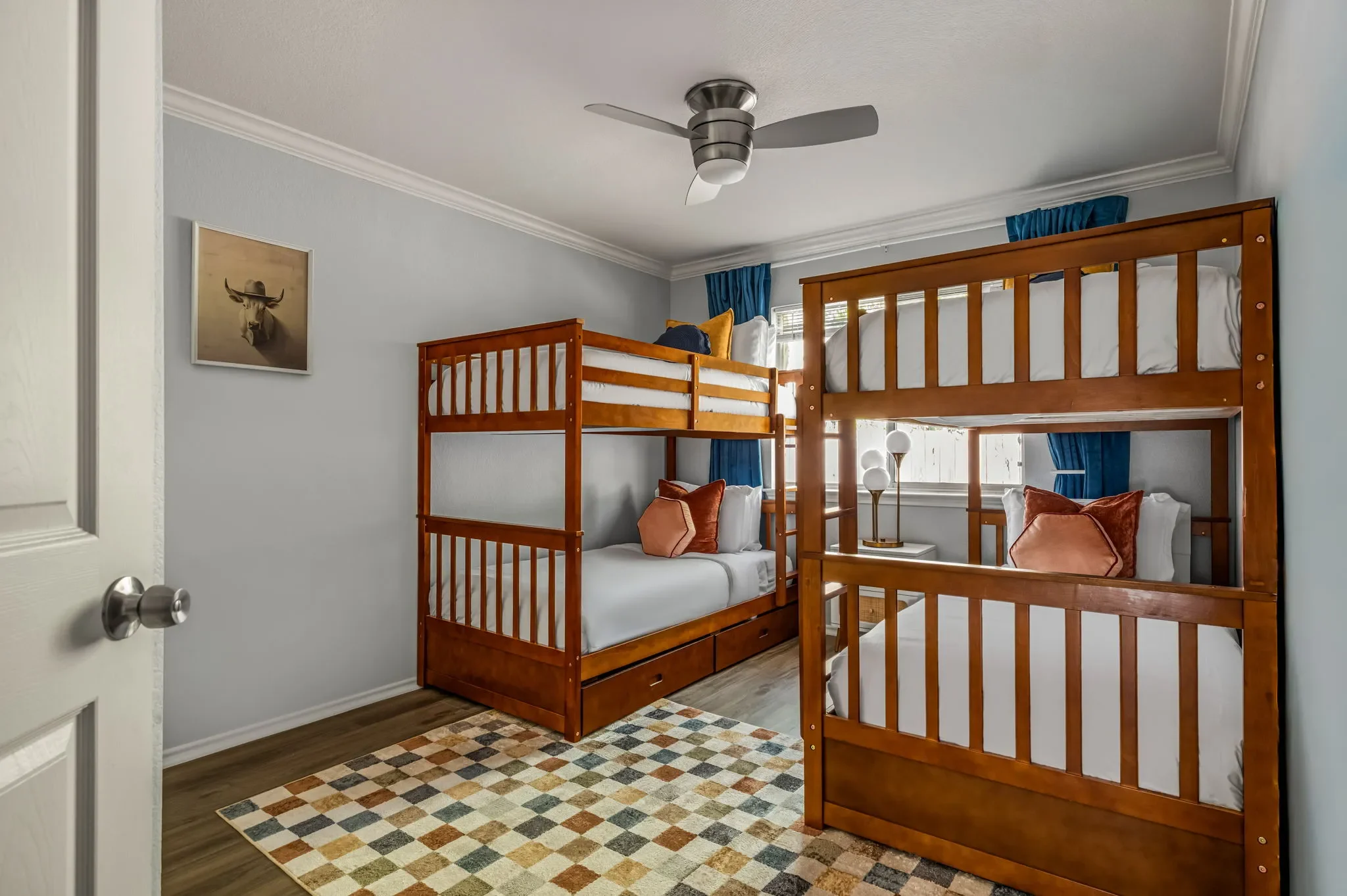 Bedroom with twin bunk beds, a colorful checkered rug, and blue floor-to-ceiling curtains.