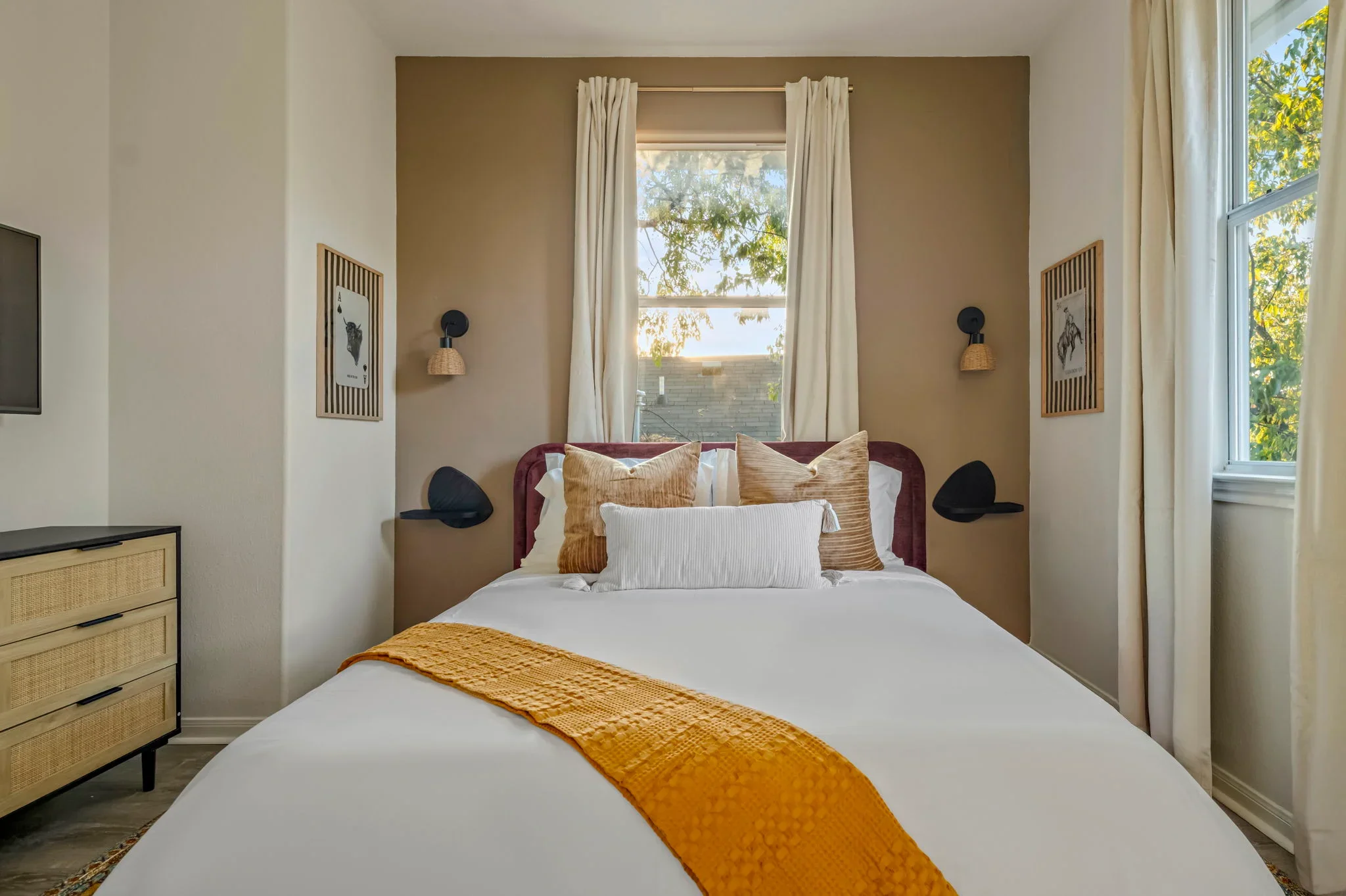Airbnb bedroom design detail with burgundy velvet headboard, tan walls, black sconces, and rattan dresser — Austin TX.