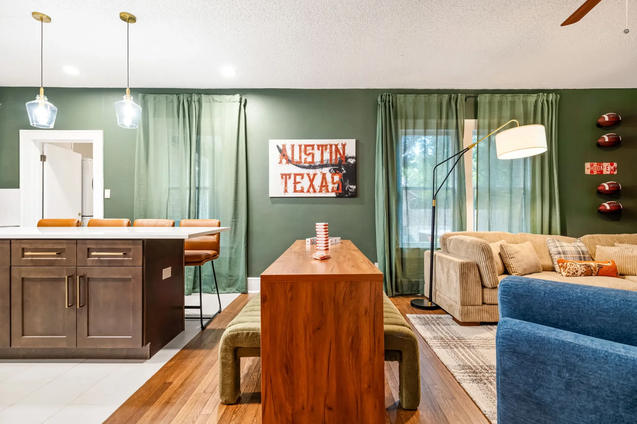 Short-term rental dining and living room design with wood dining table, dark cabinets, green walls, Austin Texas art, and football decor — Austin TX.