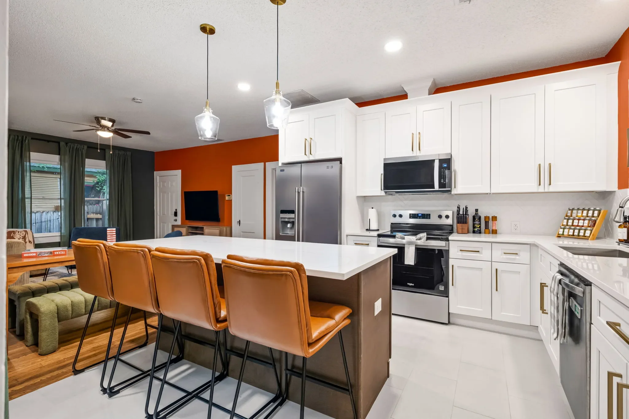 Short-term rental kitchen design with white cabinets, orange accent wall, leather bar stools, quartz island, and stainless appliances — Austin TX.