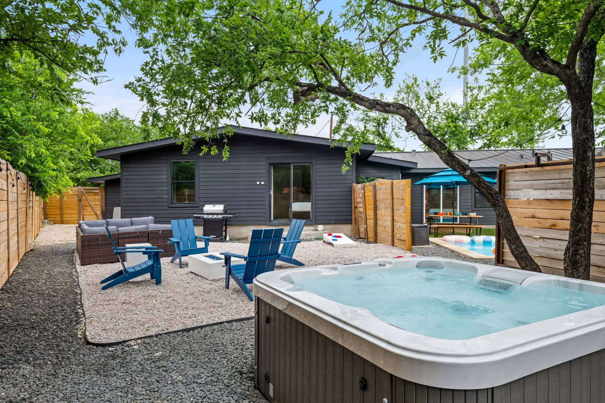 Short-term rental backyard design with hot tub, blue Adirondack chairs, gravel patio, and guest house — Austin TX.