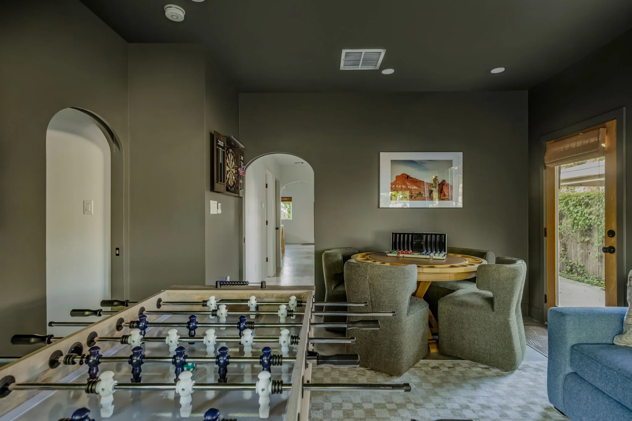 Short-term rental game room design with foosball table, round poker table, arched doorway, and olive green walls — Austin TX.