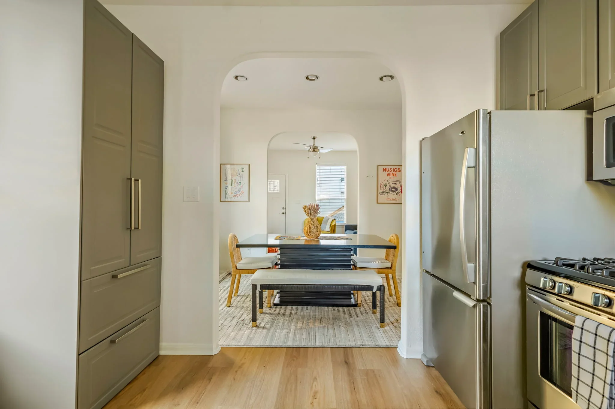 Airbnb kitchen and dining design with stainless appliances, sage cabinetry, arched doorway, and music wall art — Austin TX.