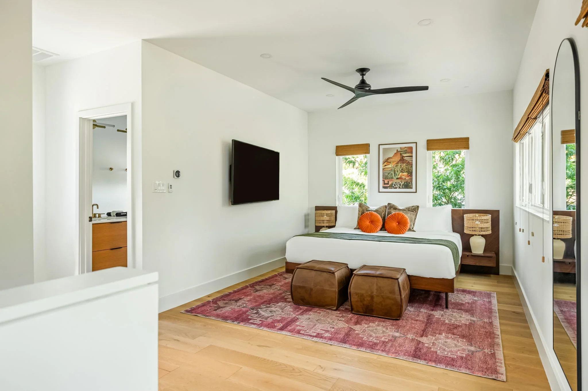 Short-term rental primary bedroom design with dark wood bed frame, leather ottomans, vintage rug, TV, and ensuite bathroom — Austin TX.
