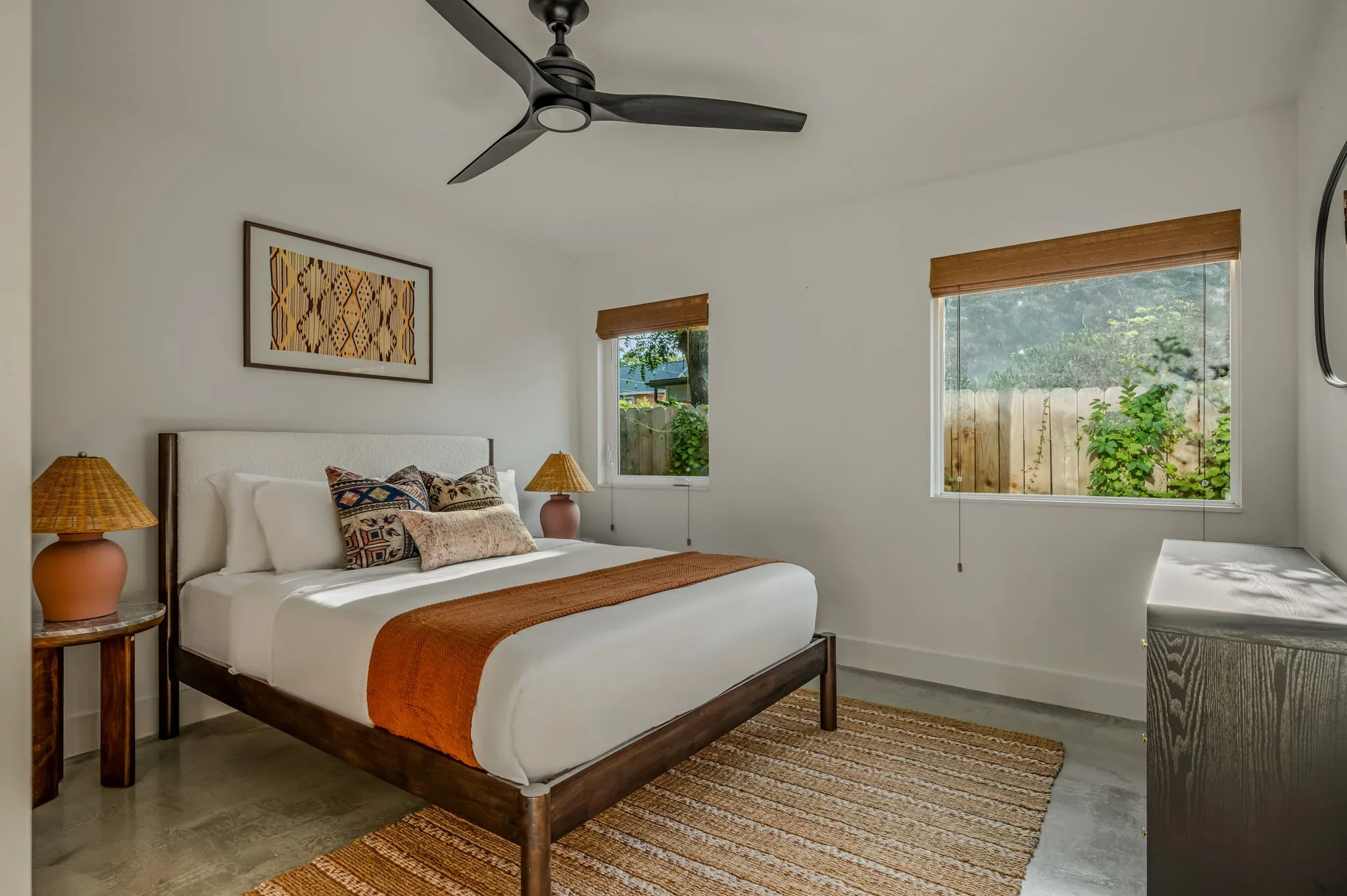 Airbnb guest bedroom design with upholstered headboard, terracotta lamp, woven lamp, kilim textile art, and orange throw — Austin TX.