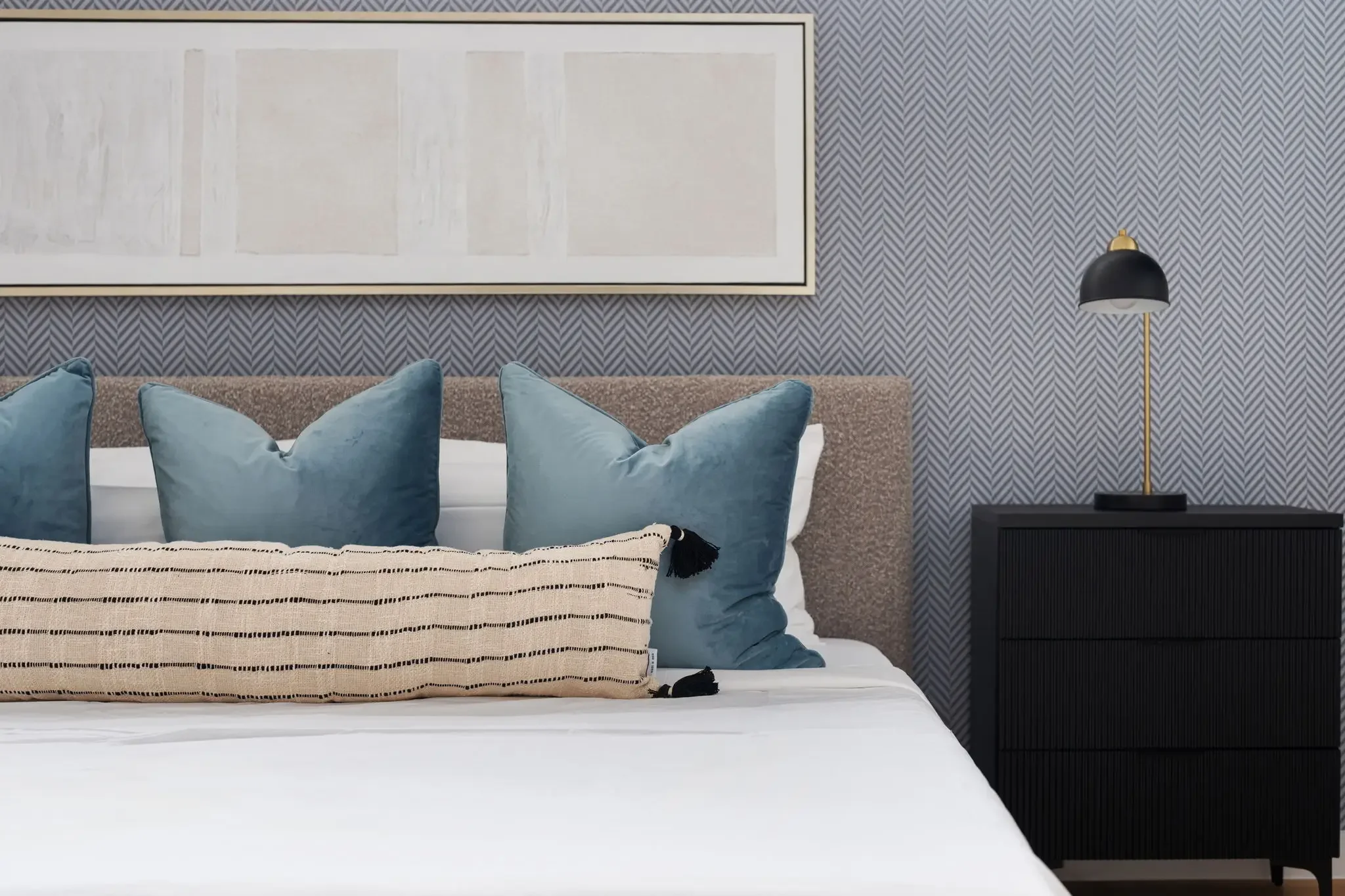 Airbnb bedroom design detail with blue herringbone wallpaper, linen headboard, teal pillows, black nightstand, and brass sconce — Austin TX.