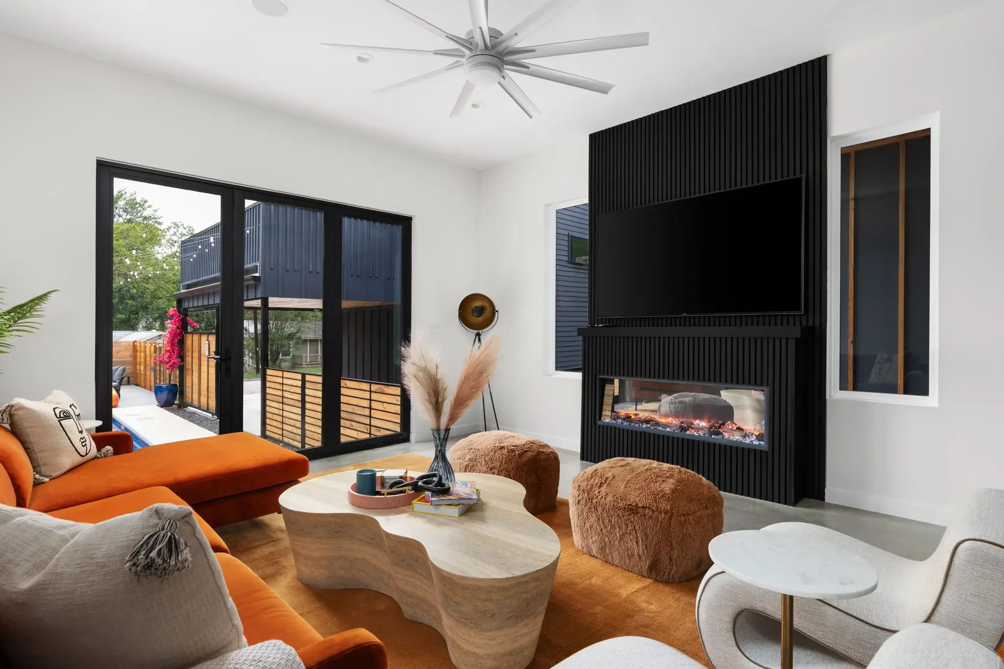 Airbnb living room design with black slat fireplace, large TV, orange sectional, fuzzy accent stool, and vaulted ceiling — Austin TX.