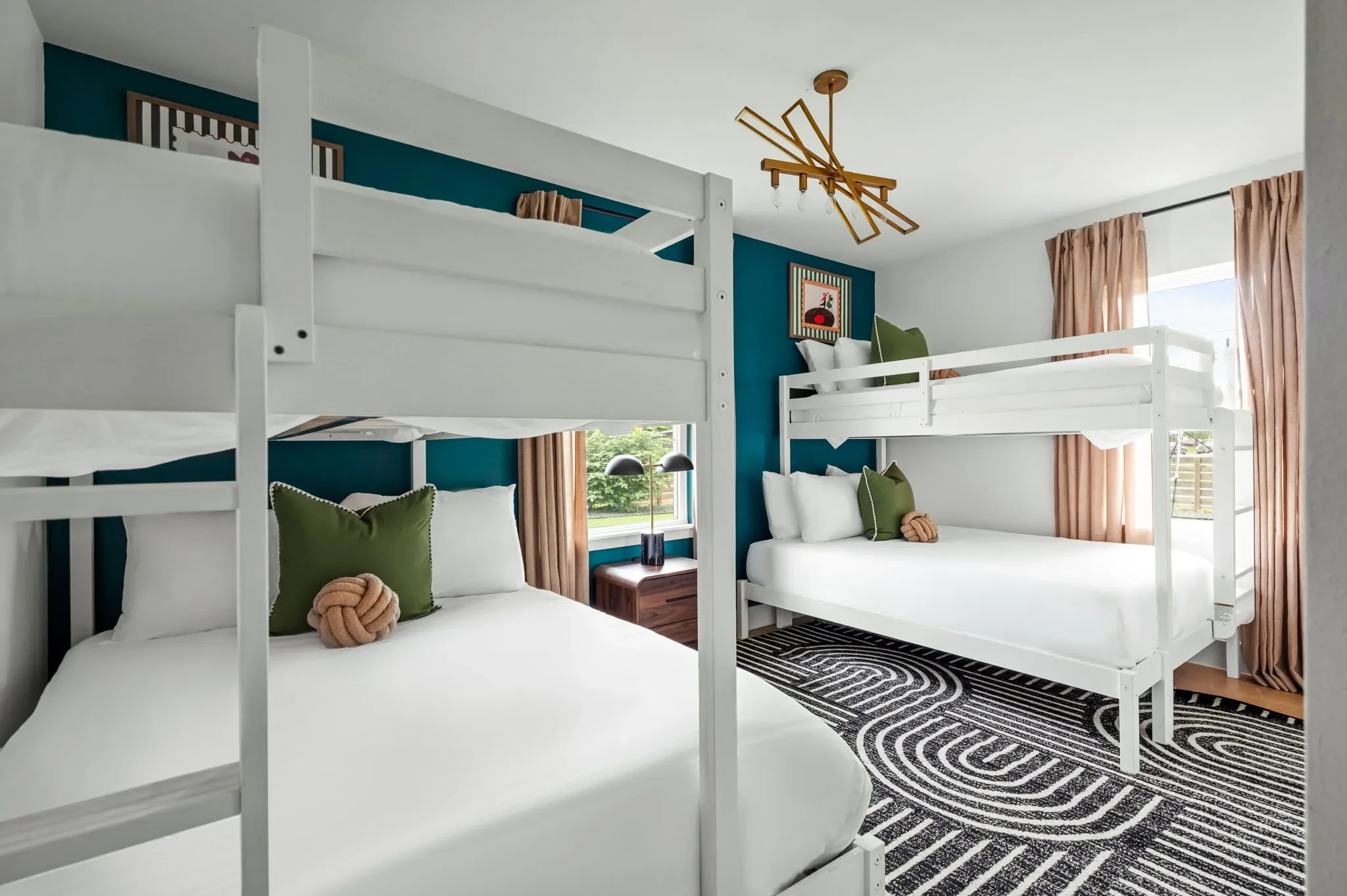 Short-term rental bunk room design with white bunk beds, teal accent wall, brass chandelier, green pillows, and graphic rug — Austin TX.