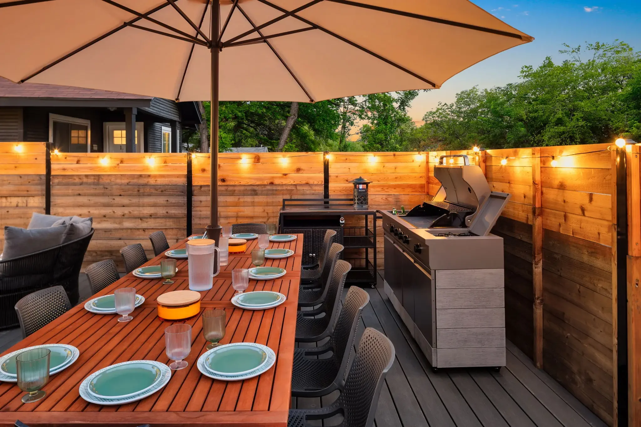Airbnb outdoor dining design with set table for ten, large umbrella, built-in grill station, and string lights — Austin TX.