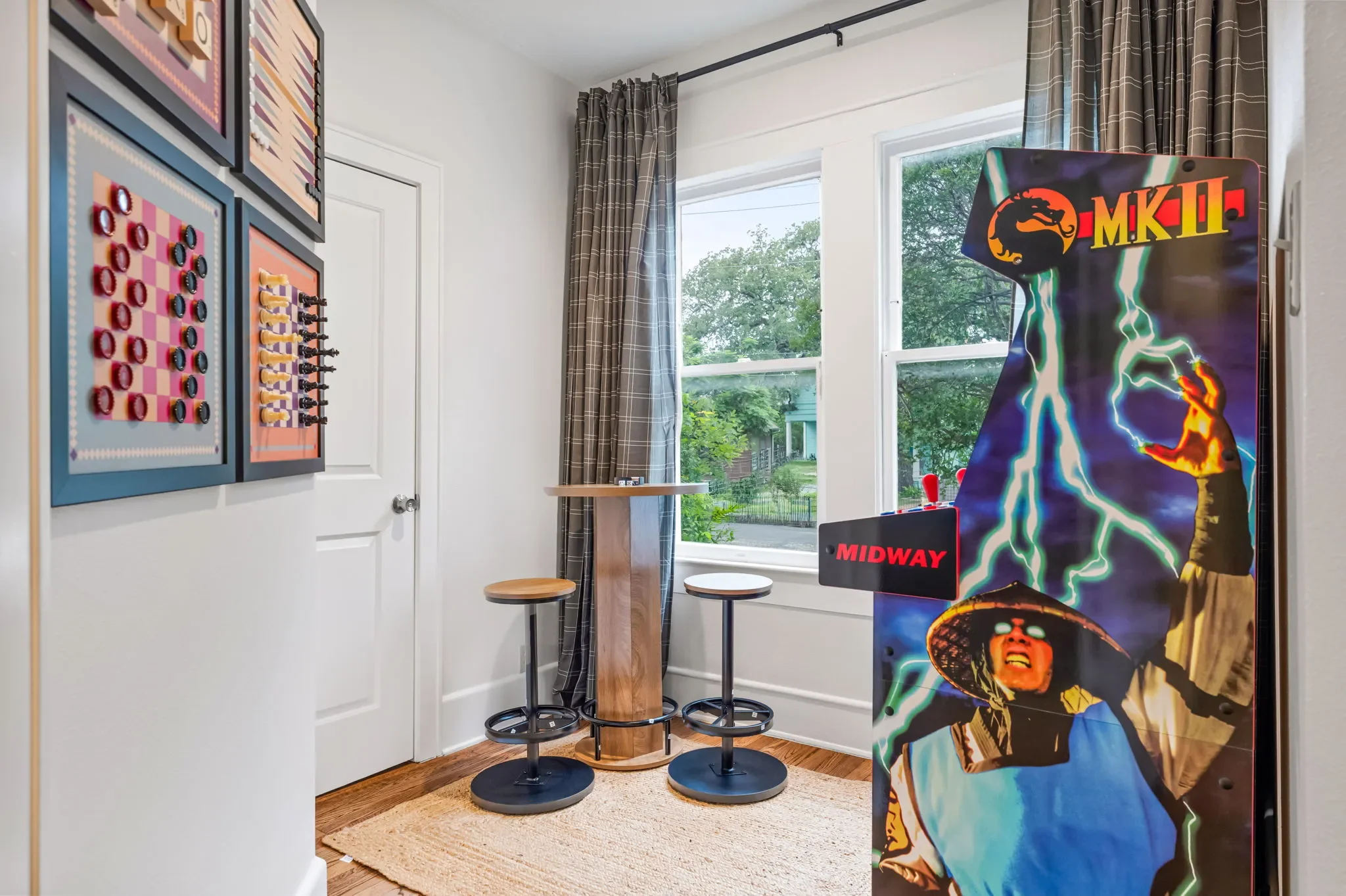 Short-term rental game room design with Mortal Kombat arcade poster, framed board game art, and bar stools — Austin TX.