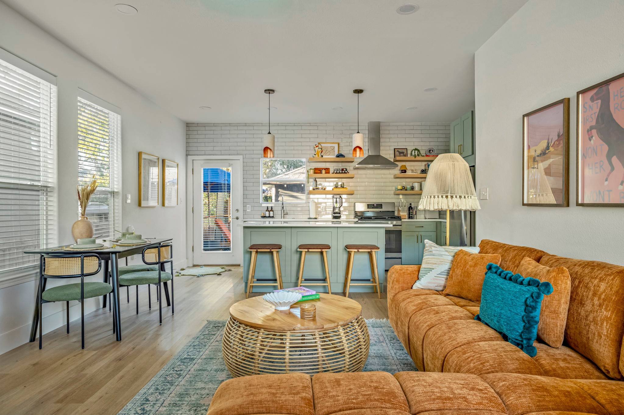 Austin short-term rental interior showing a combined living room and renovated kitchen with island seating, dining area, and sage green furnishings.