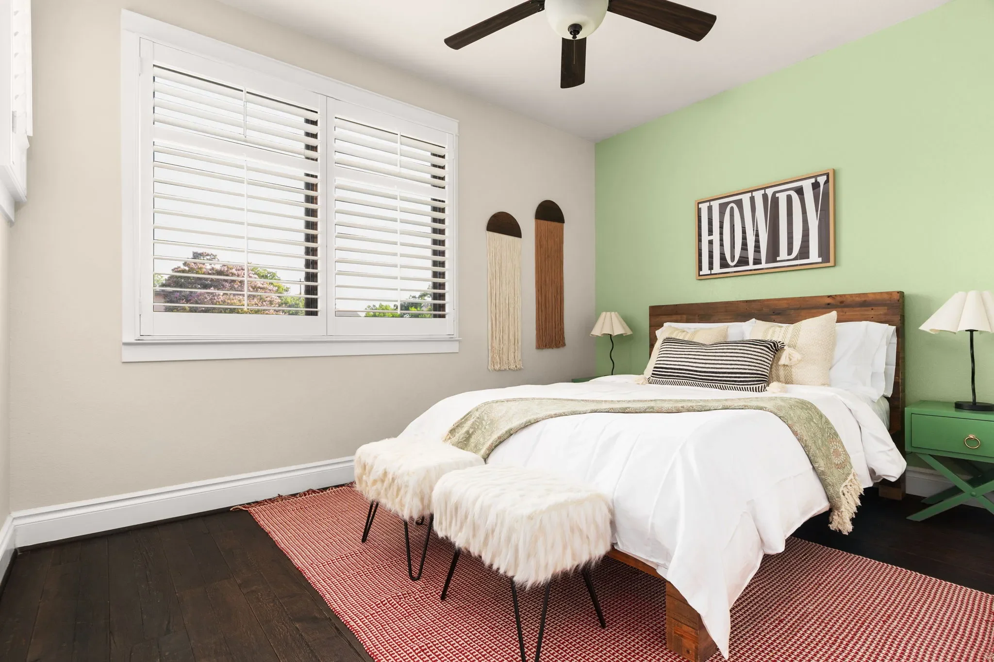 Bedroom with mint green wall paint, “Howdy” wall art, fur accent stools, and rustic wooden wall decor and nightstands.