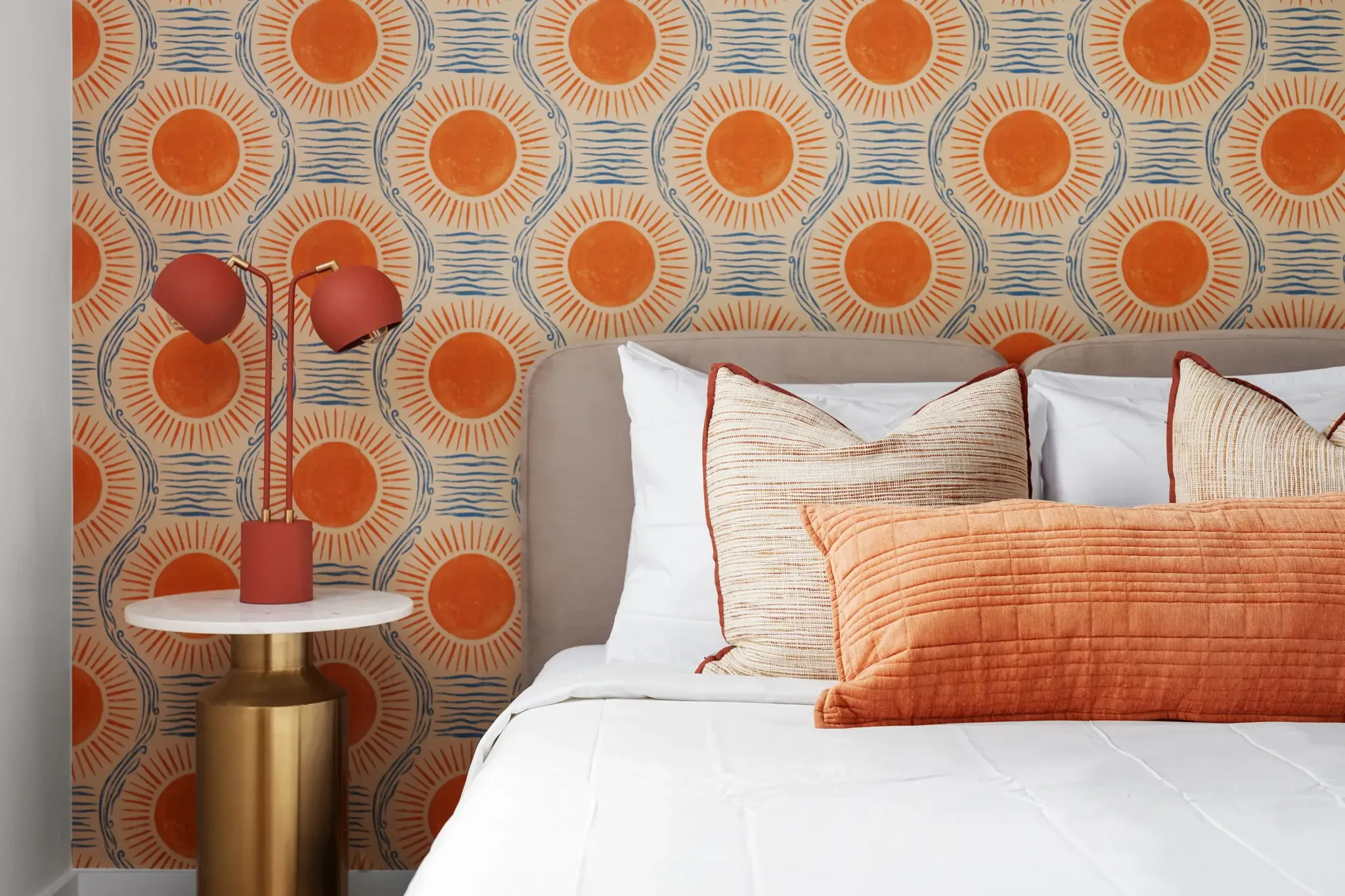 Short-term rental bedroom design detail with bold retro sun wallpaper, linen headboard, orange pillows, and terracotta lamp — Austin TX.