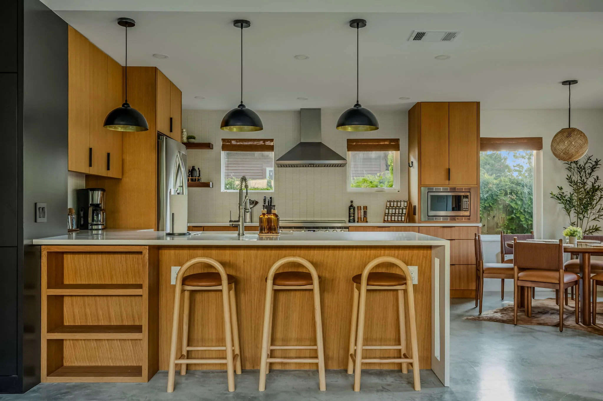 Short-term rental kitchen design with warm wood cabinetry, white quartz island, arched bar stools, black pendant lights, and subway tile backsplash — Austin TX.