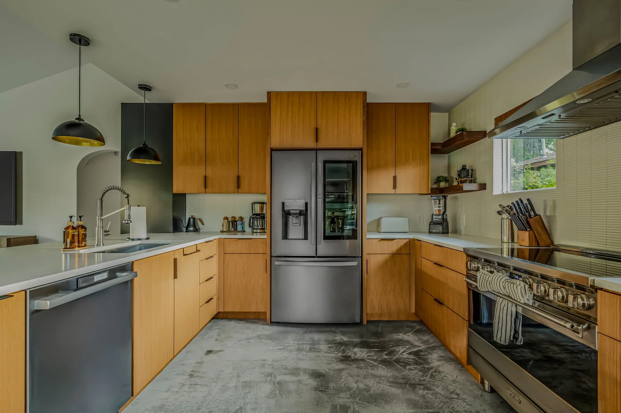 Airbnb kitchen design with warm wood cabinetry, stainless appliances, white quartz counters, and concrete floors — Austin TX.