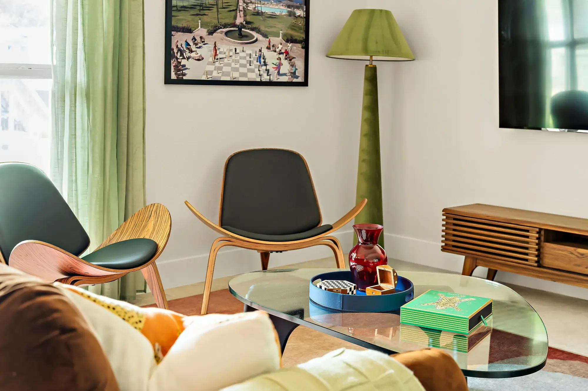 Airbnb sitting room design detail with mid-century shell chairs, glass coffee table, green lamp, and chess wall art — Austin TX.
