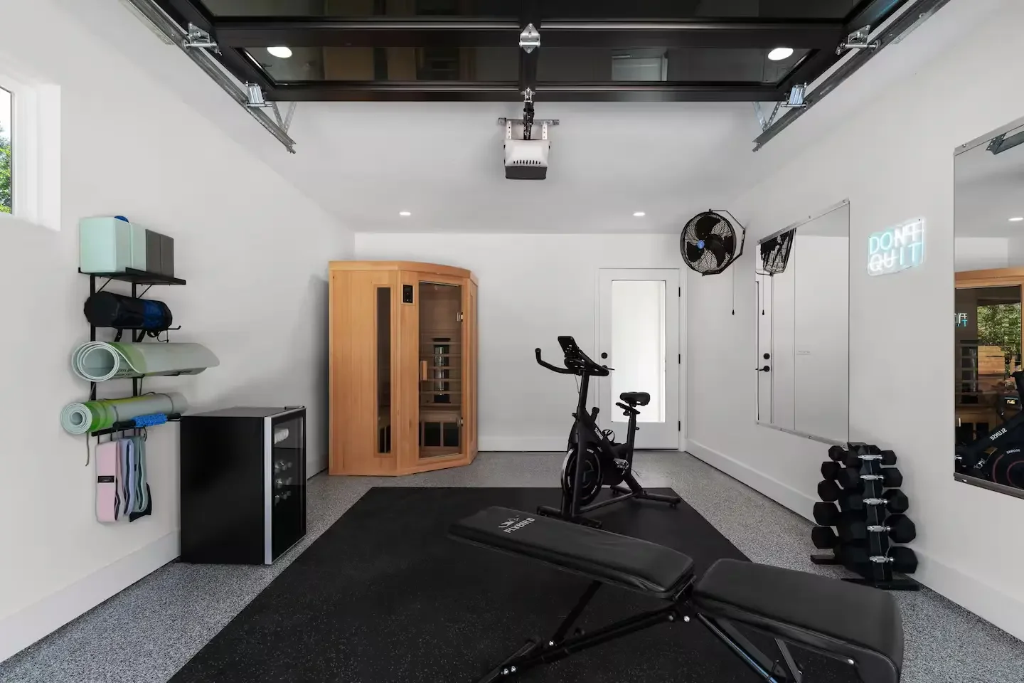 Home gym in a converted garage with sauna, weights, yoga gear, and neon wall signage.