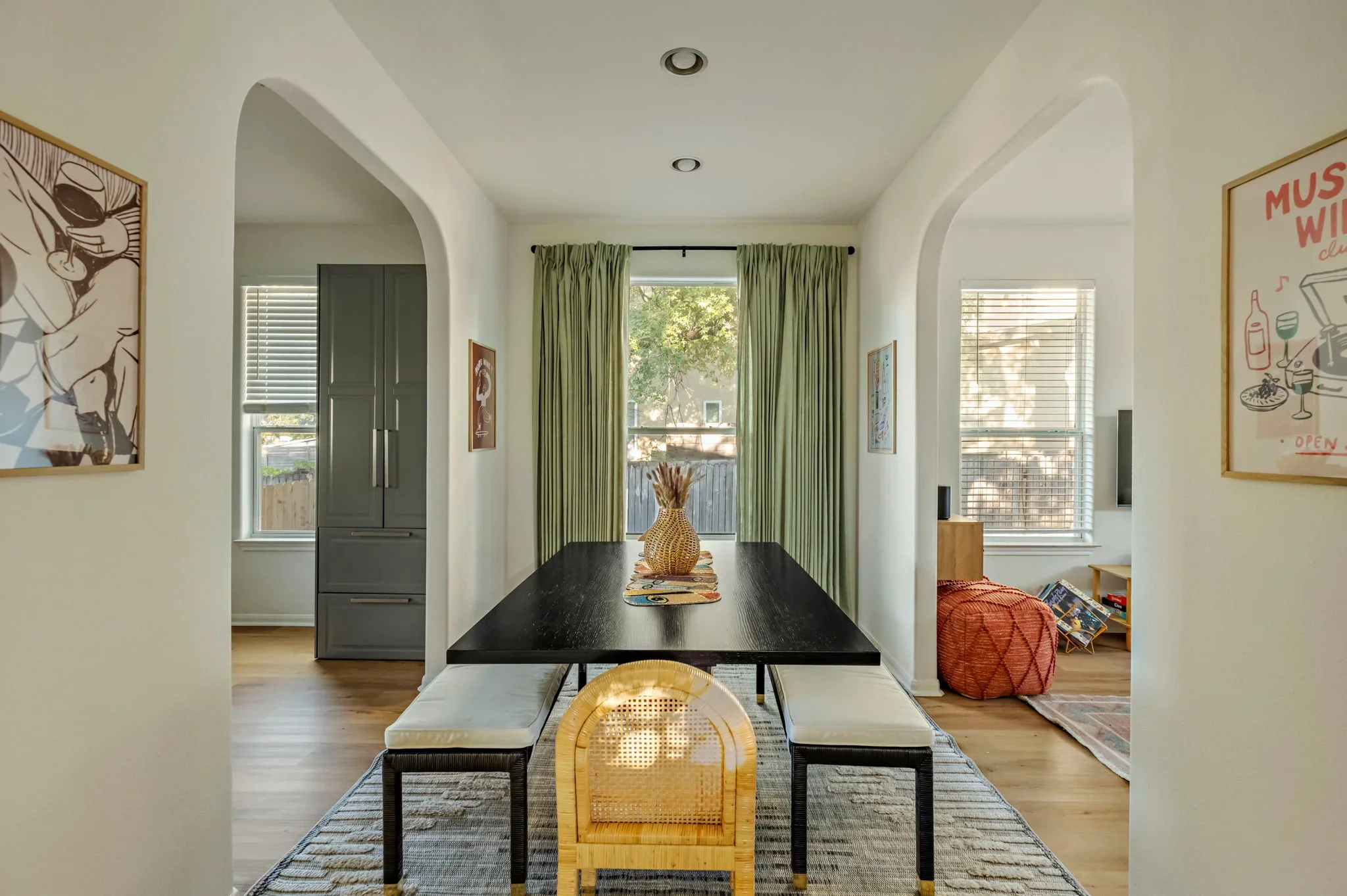 Short-term rental dining room design with black wood table, sage green curtains, arched doorways, and pop art prints — Austin TX
