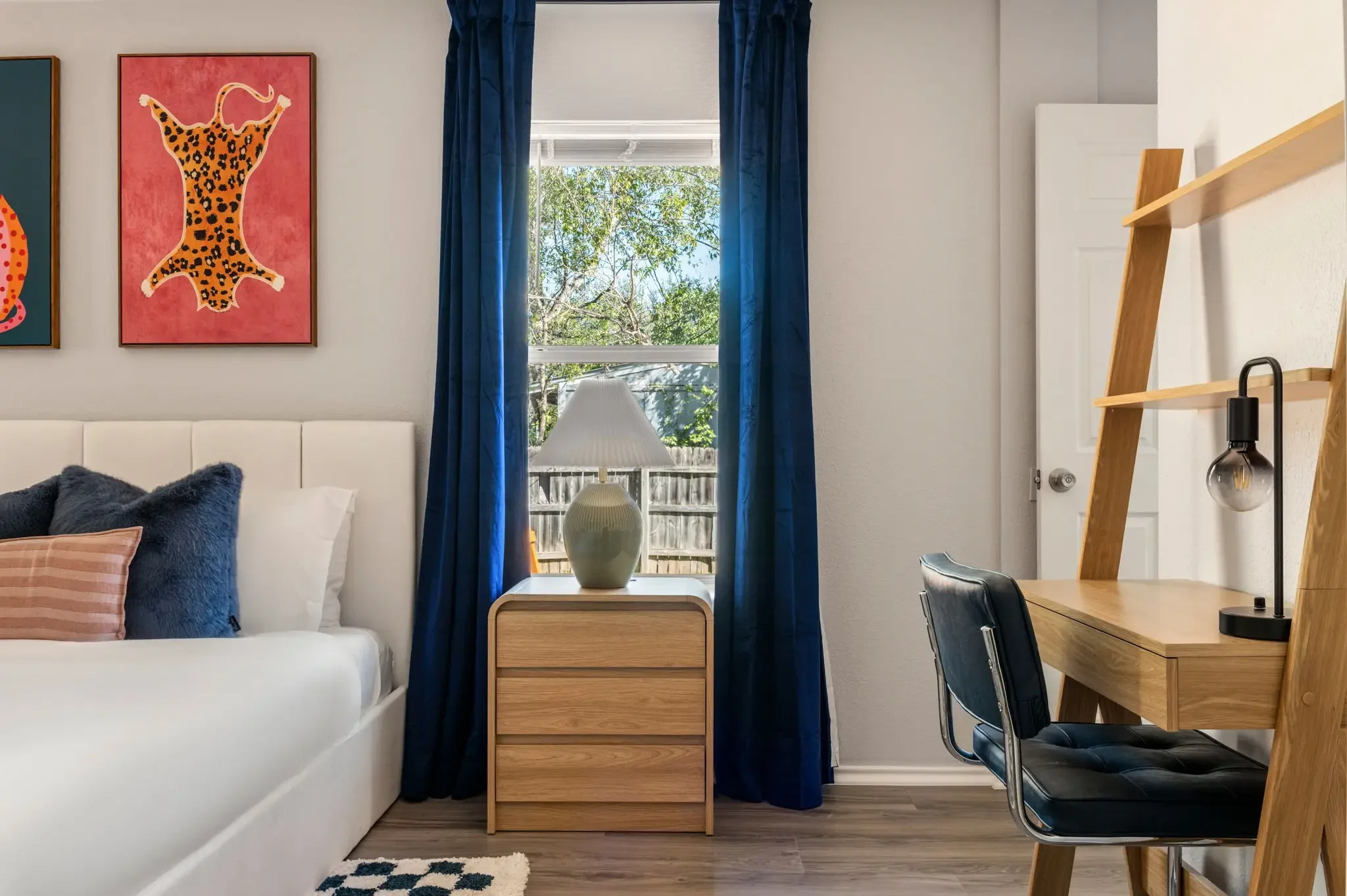 Airbnb bedroom design with navy curtains, leopard wall art, wood nightstand, and leaning desk — Austin TX.