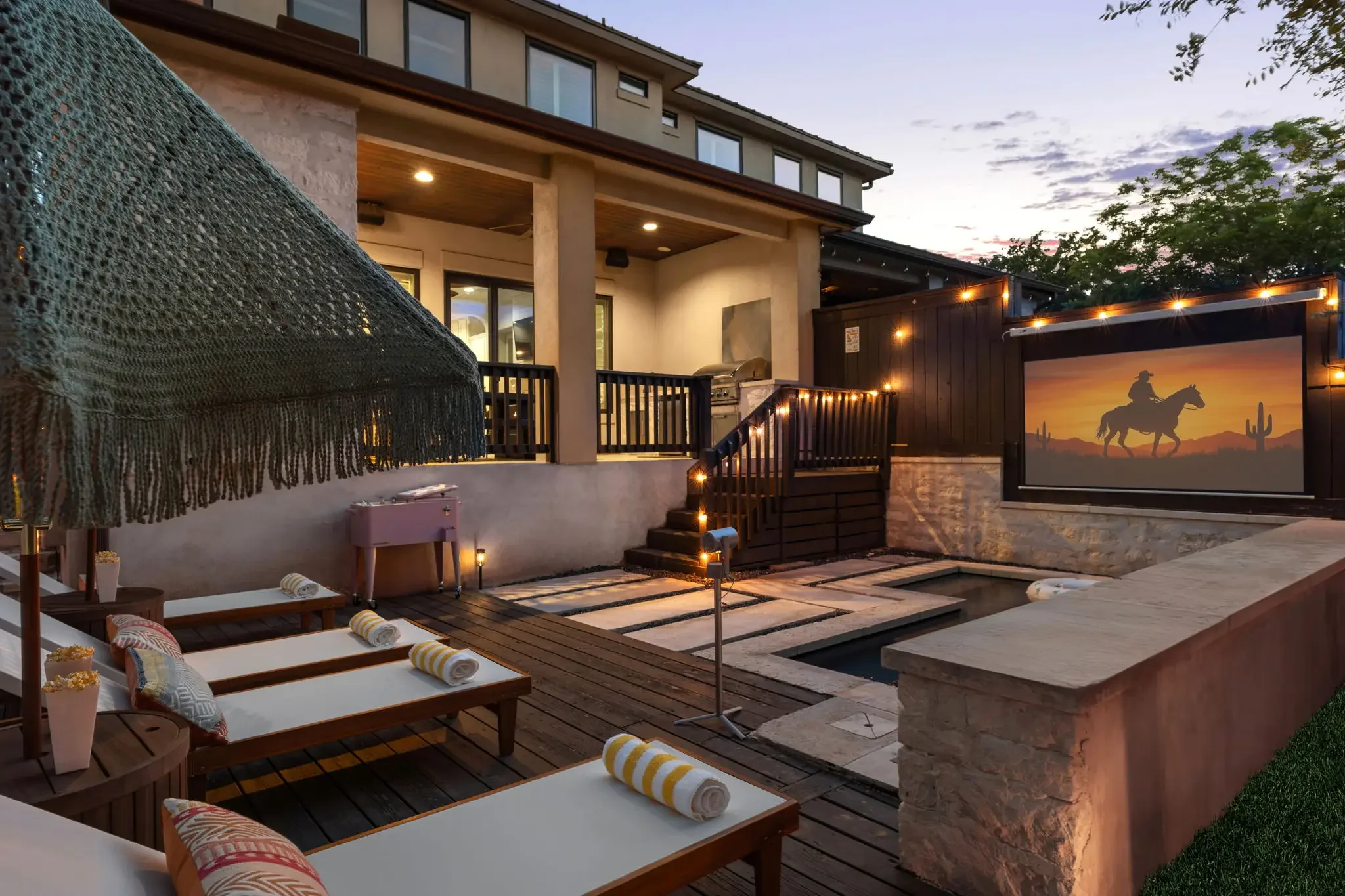 Airbnb outdoor design with pool, lounge chairs, macrame umbrellas, and outdoor cinema screen at sunset — Austin TX.