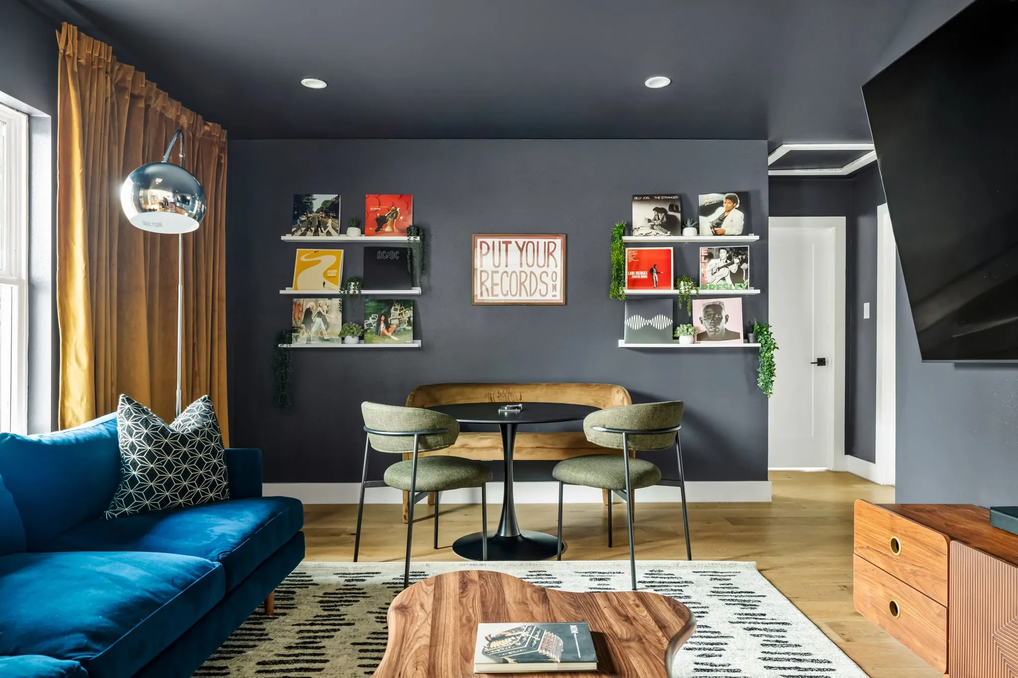 Airbnb lounge room design detail with Put Your Records On wall art, vinyl shelving, blue sofa, and bistro dining table — Austin TX.