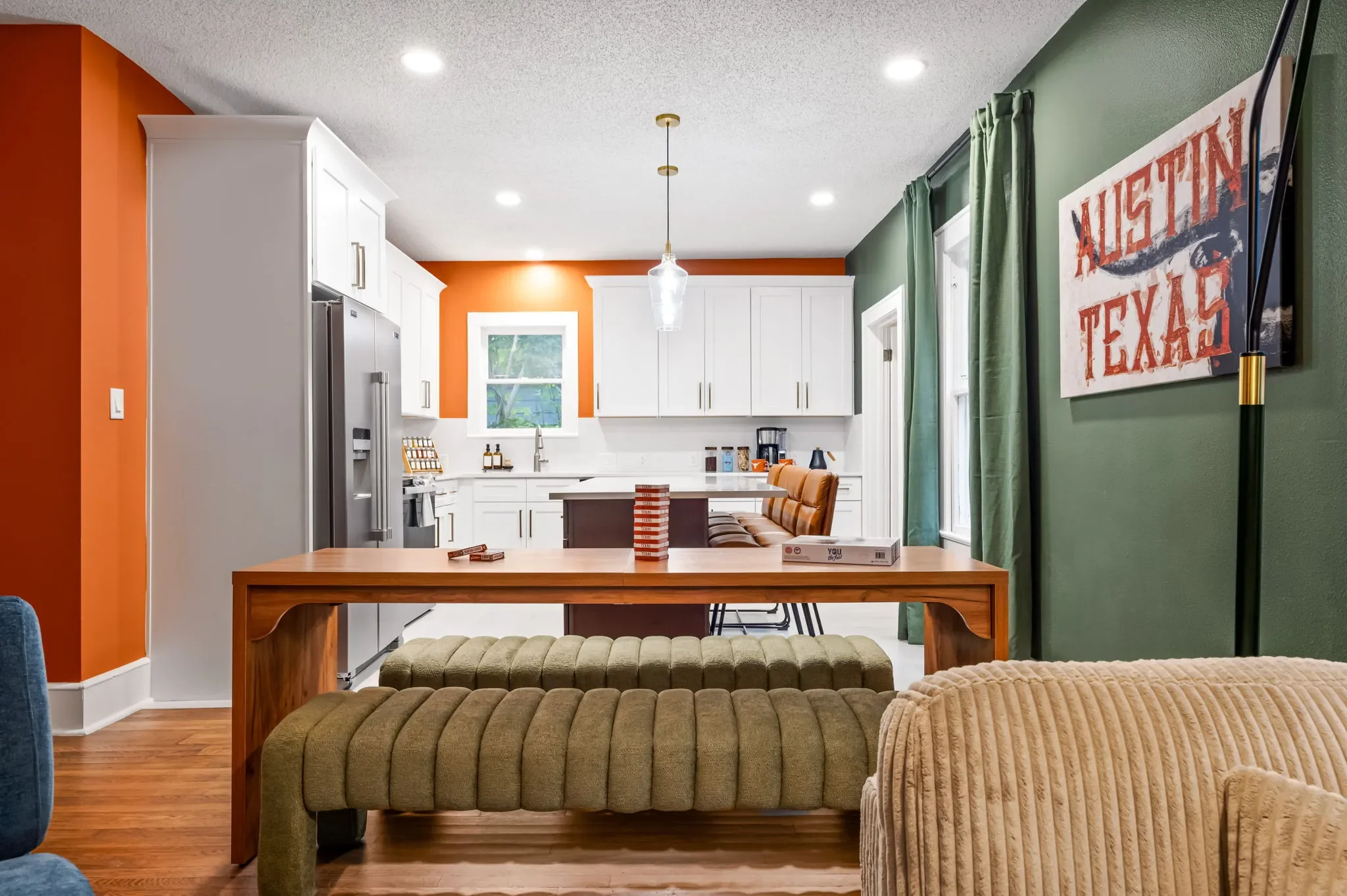 Airbnb open plan design with orange accent wall, white kitchen, wood dining table, green walls, and Austin Texas wall art — Austin TX.