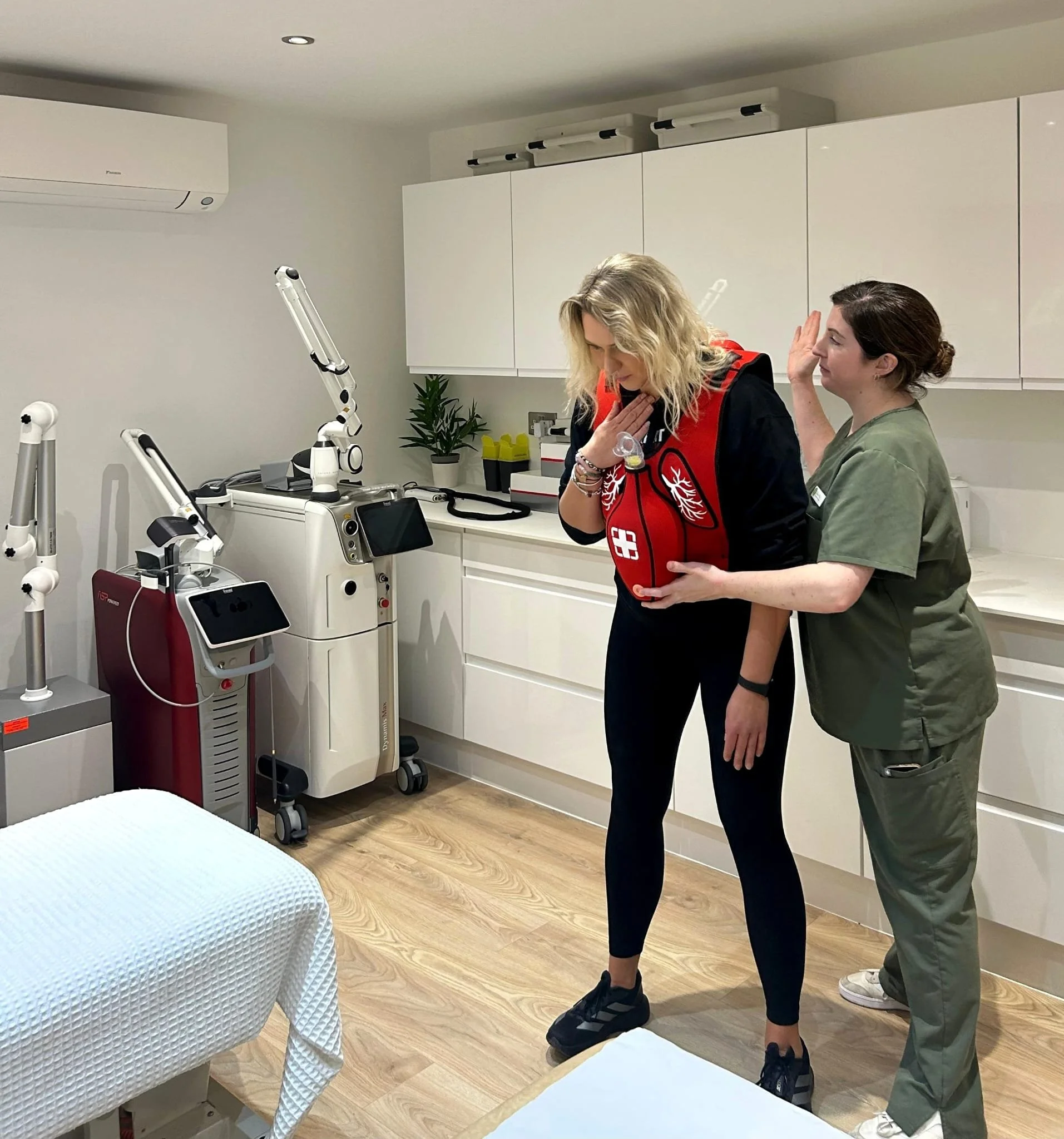 A woman receiving CPR training from a nurse in a medical room with Lumecca and other medical devices.