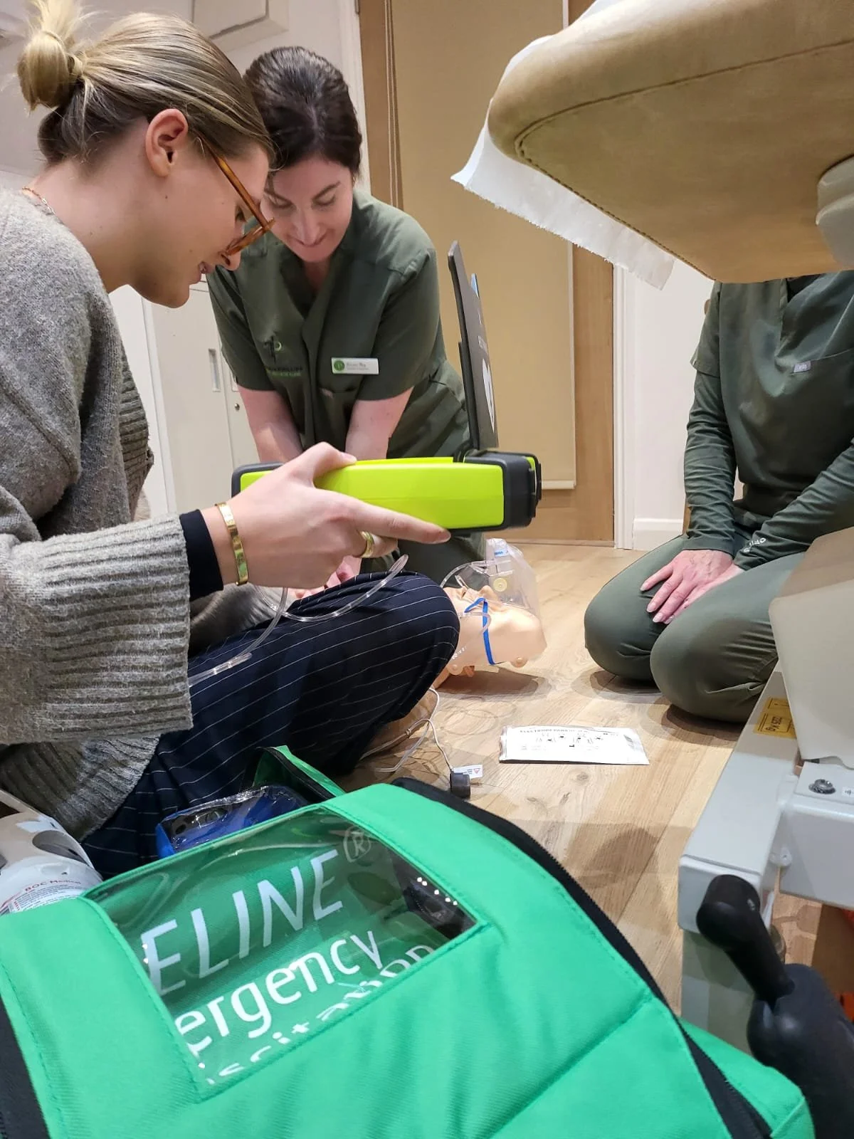 Medical training scenario with two healthcare professionals practicing CPR or airway management on a mannequin, surrounding emergency medical equipment and supplies.