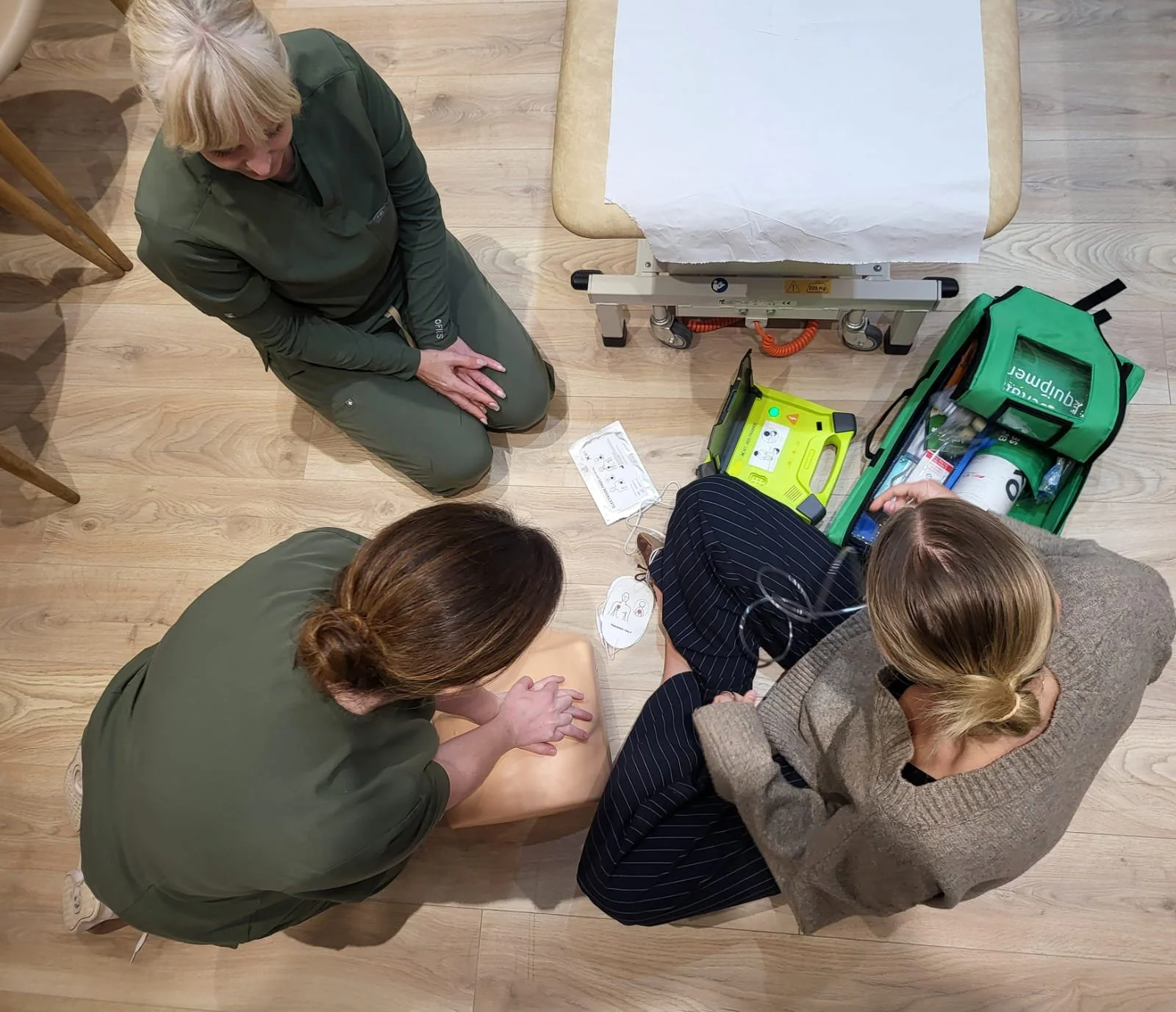 Three women practicing CPR on a training manikin with medical equipment nearby.
