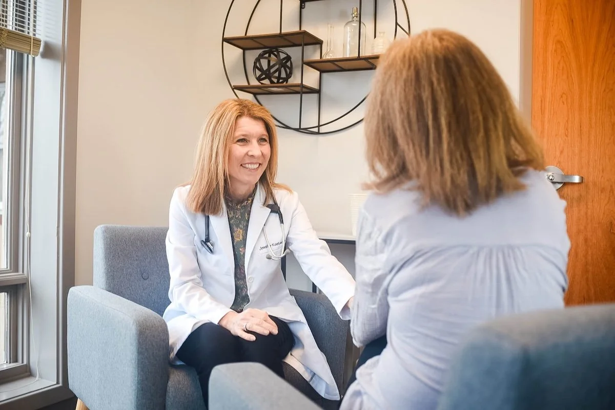 Dr. Jennifer Kostacos talking to a female patient in a consultation room.