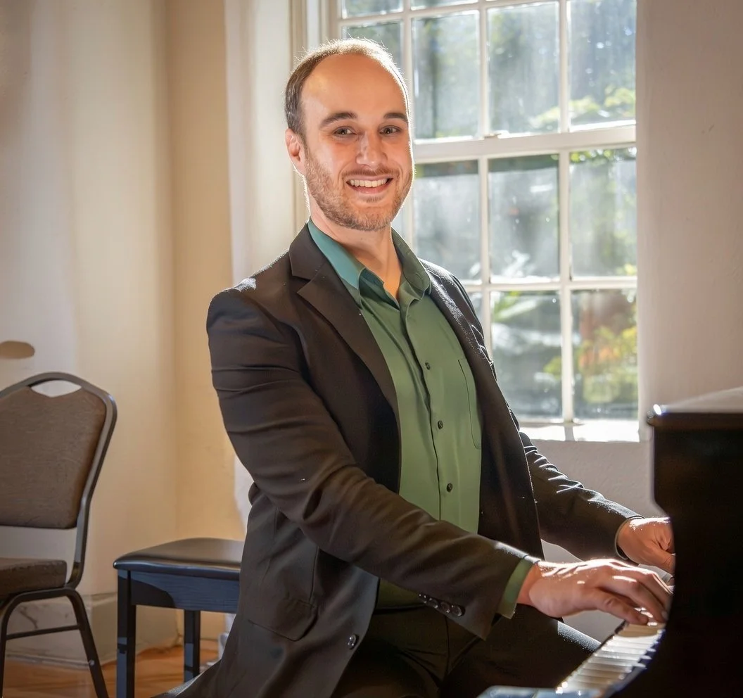 A Glenview, Northbrook, Wilmette, Skokie, and Morton Grove IL bass, guitar and tuba instructor poses in a suit for Avant-garde music that offers lessons in your home with sunlight coming through a window.