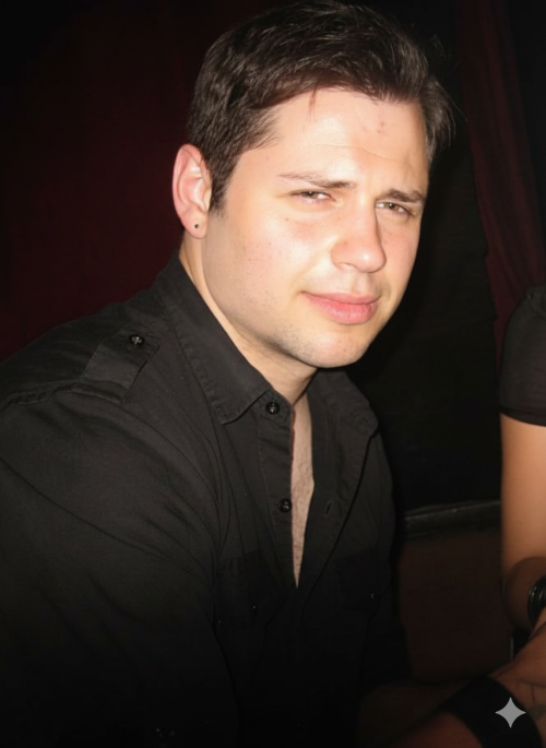 A guitar instructor for lessons in your home for Chicago northern suburbs poses, wearing a black shirt, sitting against a dark background.