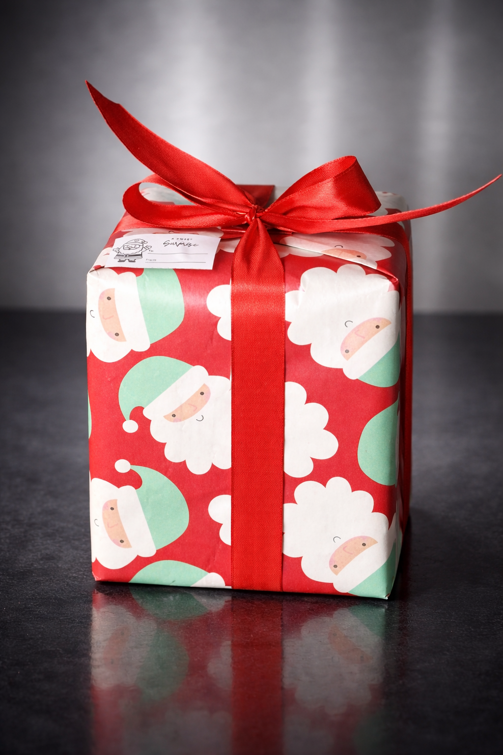A Christmas gift wrapped in festive paper featuring Santa Claus with a red background, decorated with a large red satin ribbon tied in a bow on top.
