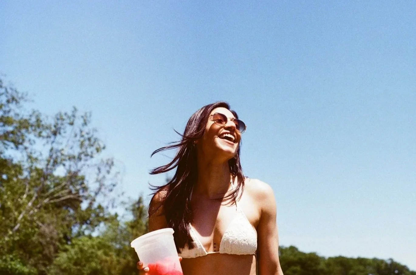 a young woman smiling in the sun with a healthy beverage and fitness routine