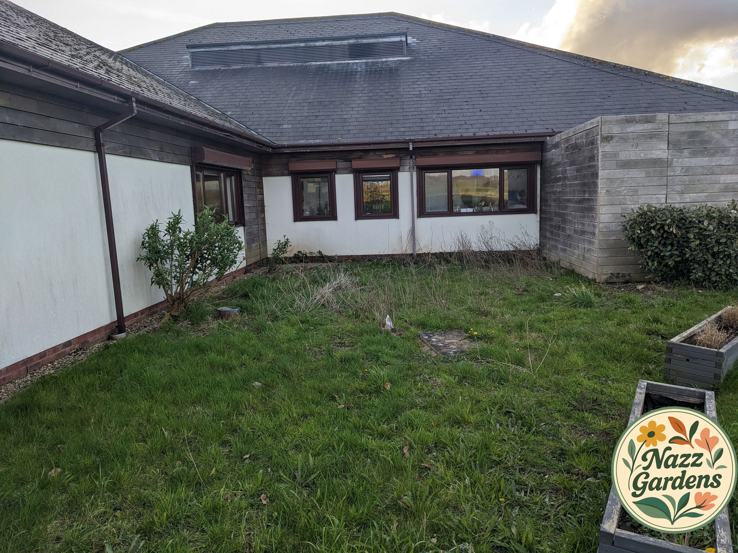 Yard with overgrown grass, small bush, and empty flower pots near a clubhouse with white and wood exterior walls and multiple windows.